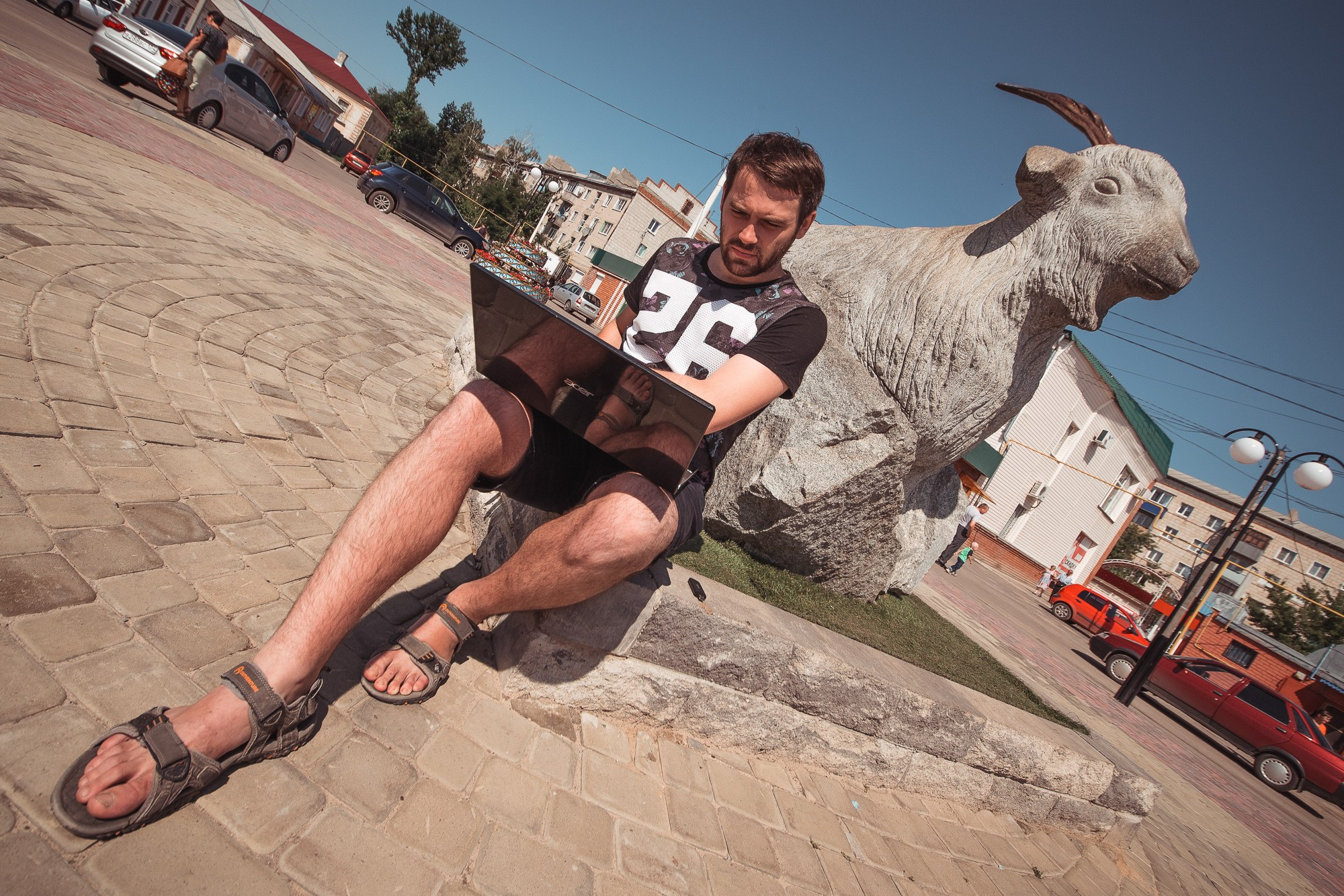 Сергей Стукалов сидит у памятника козе-кормилице с ноутбуком