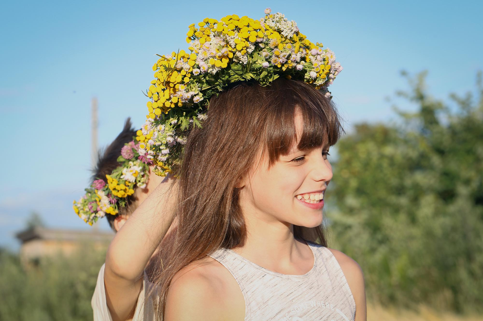 мальчик надевает на голову темноволосой девочке желтый цветочный венок