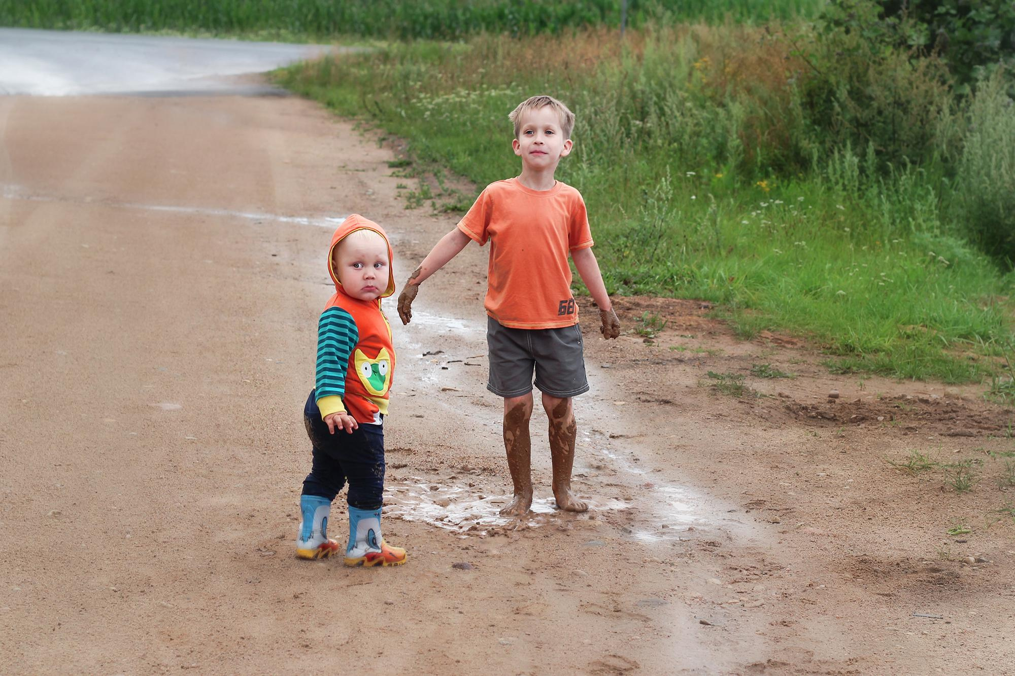 два мальчика в оранжевой одежде идут по луже в деревне