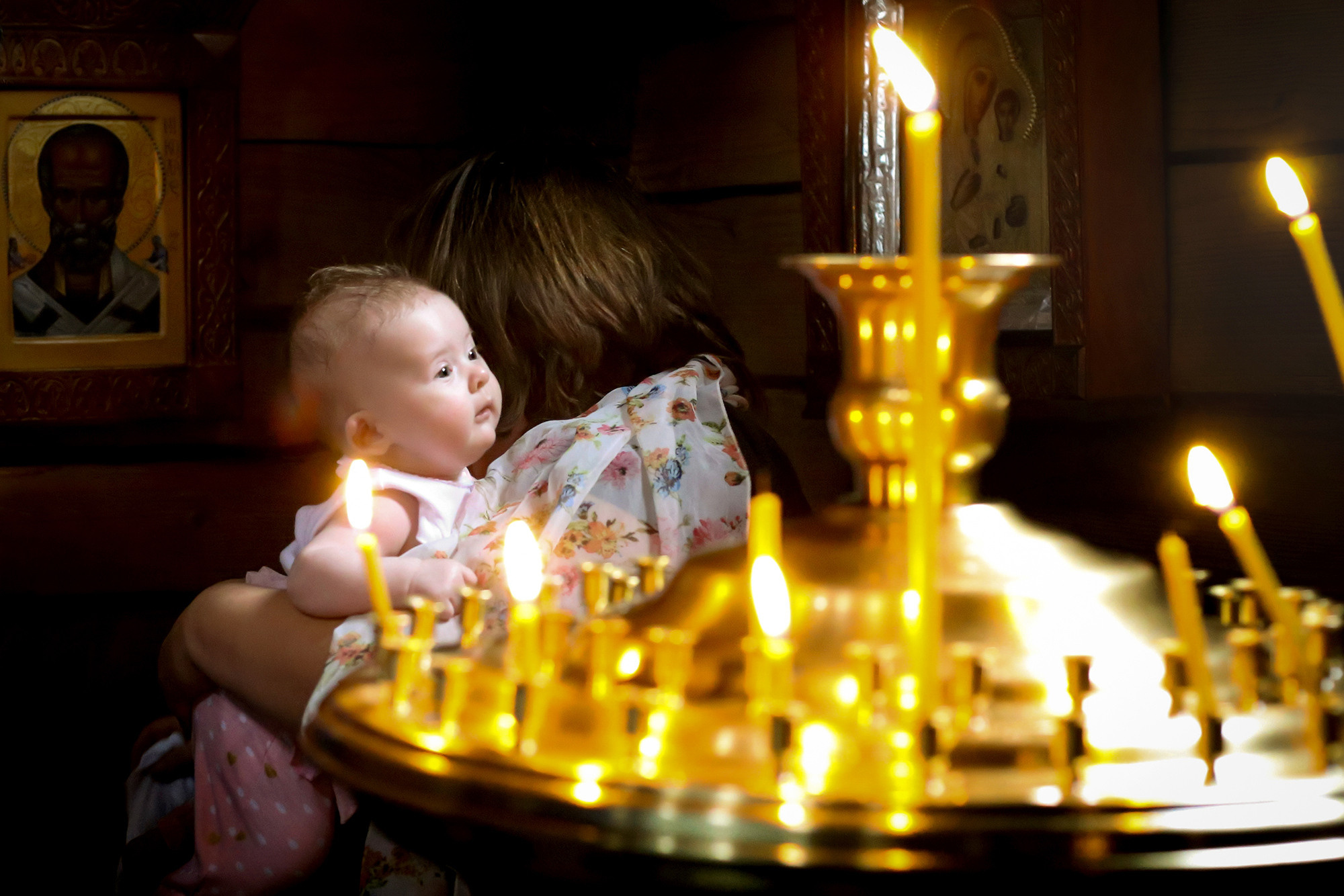 маленький ребенок в храме Божьем смотрит сквозь горящие свечи