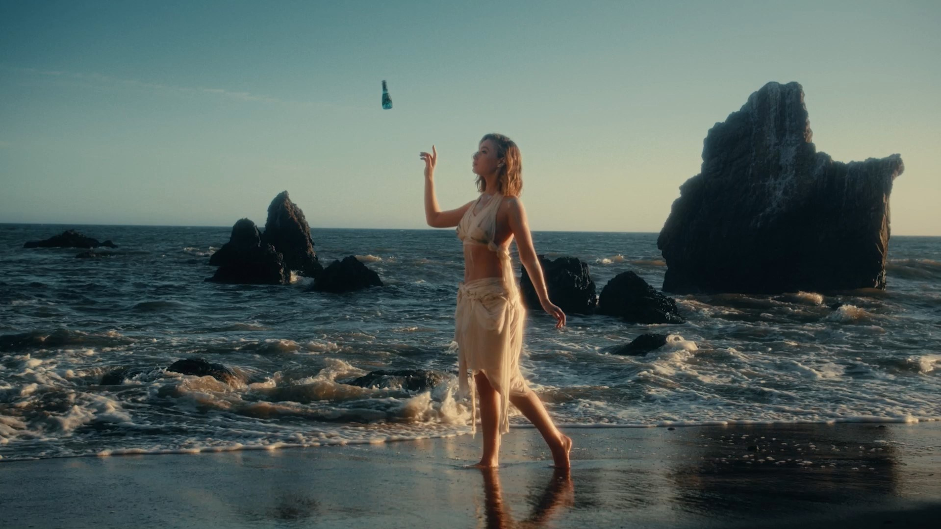 Model walking along a beach at sunset, exuding elegance in a fashion editorial shoot.