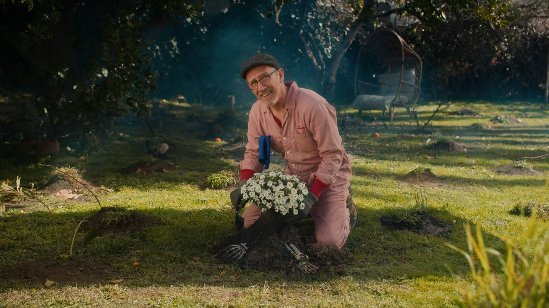 Elderly man kneeling in a garden with flowers, smiling and creating a warm, approachable mood.