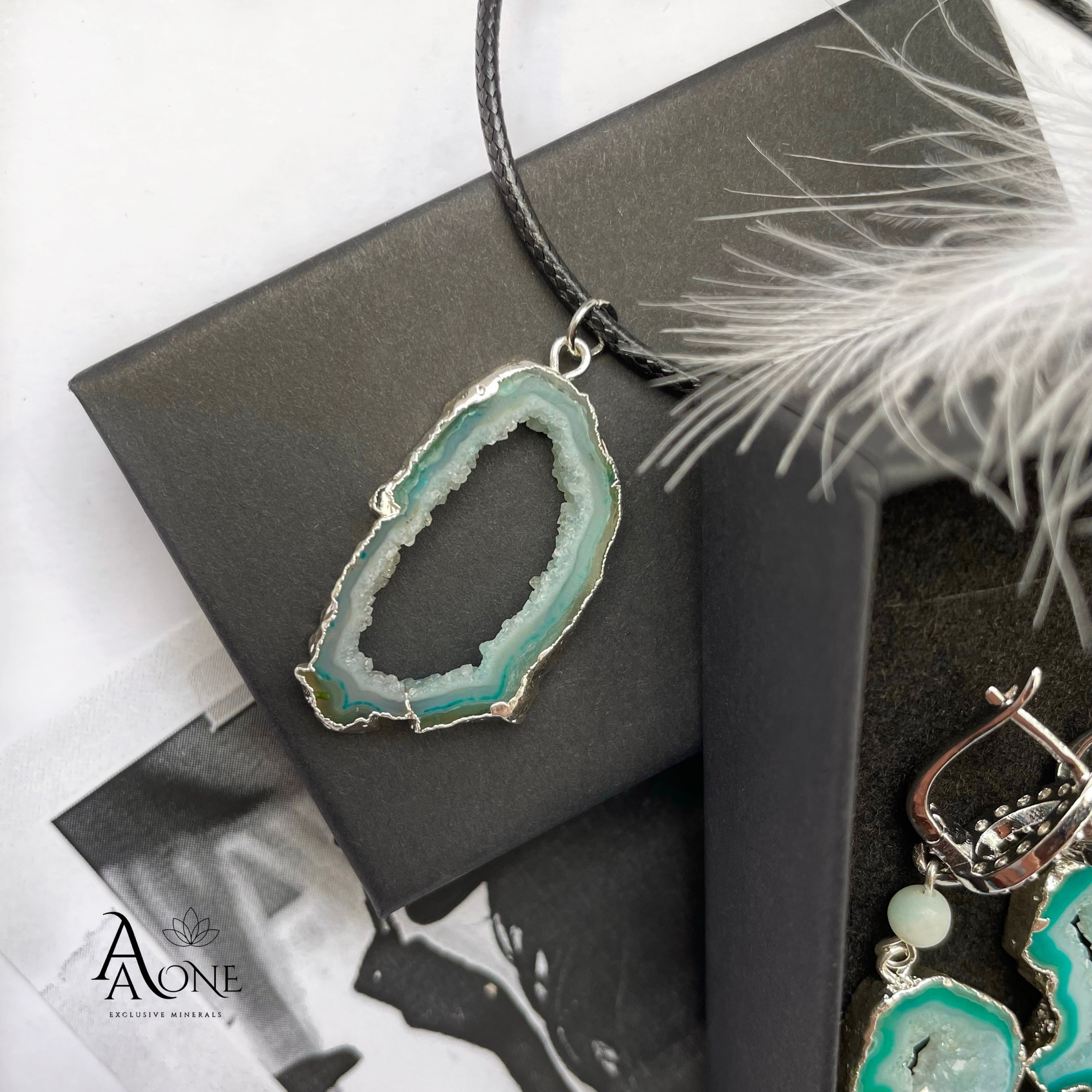 Зелёный кулон из Агата на чёрной верёвке лежит на чёрной коробочке