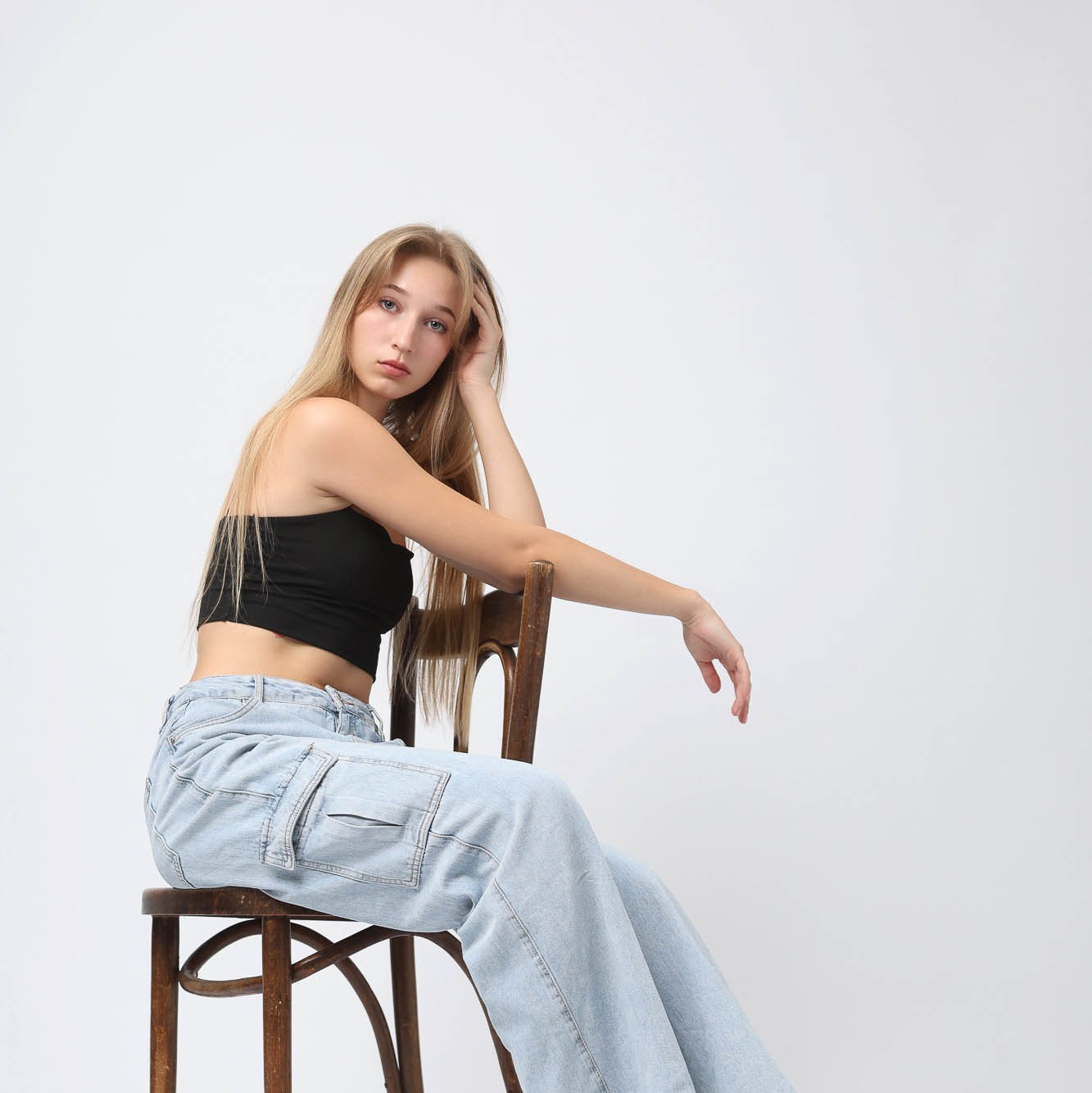 Модель на белом фоне в джинсах сидит на стуле