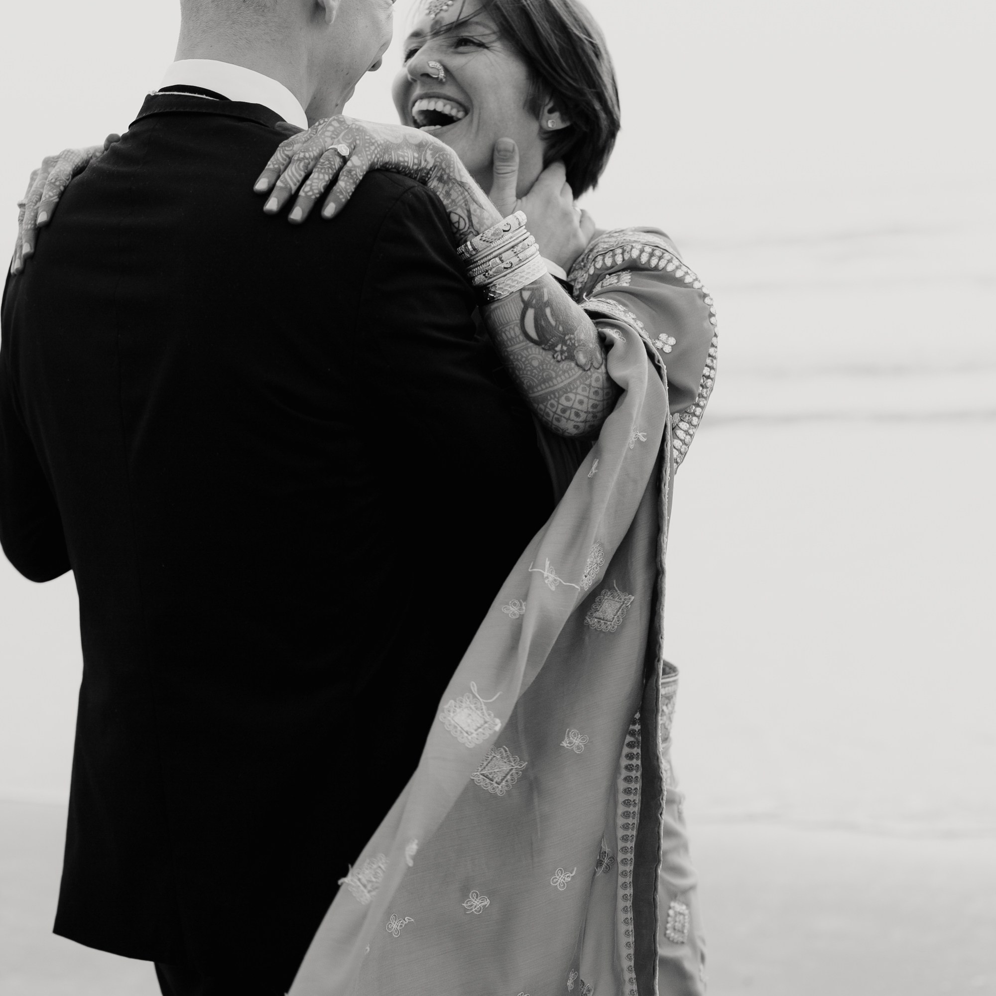 Пара обнимается и смеётся на фоне светлого неба. Эмоциональная черно-белая фотография, отражающая любовь и радость в отношениях. A couple embracing and laughing against a bright sky background. Emotional black-and-white photograph capturing love and joy in a relationship.