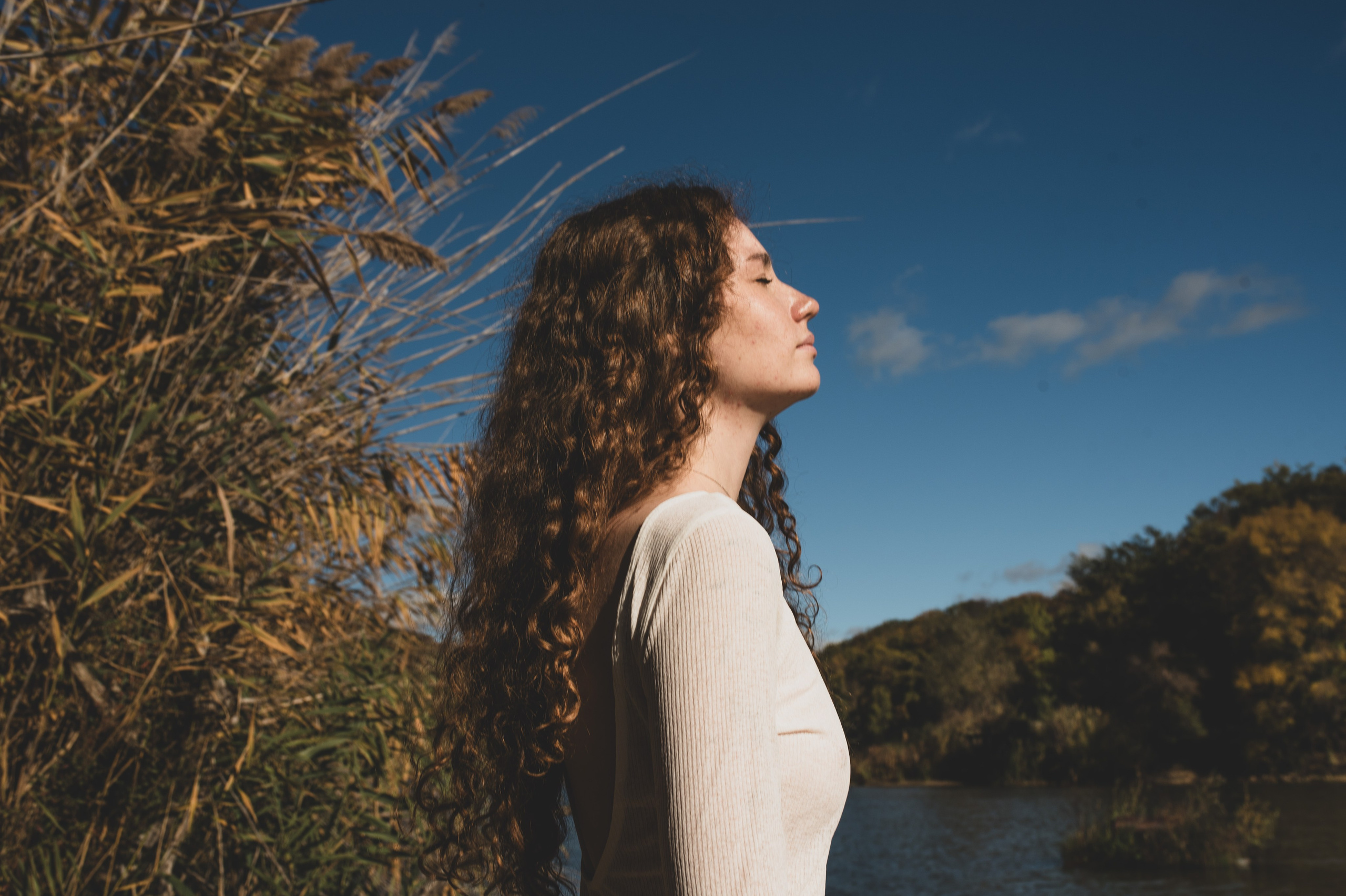 Девушка на природе с закрытыми глазами в белом платье в солнечный день