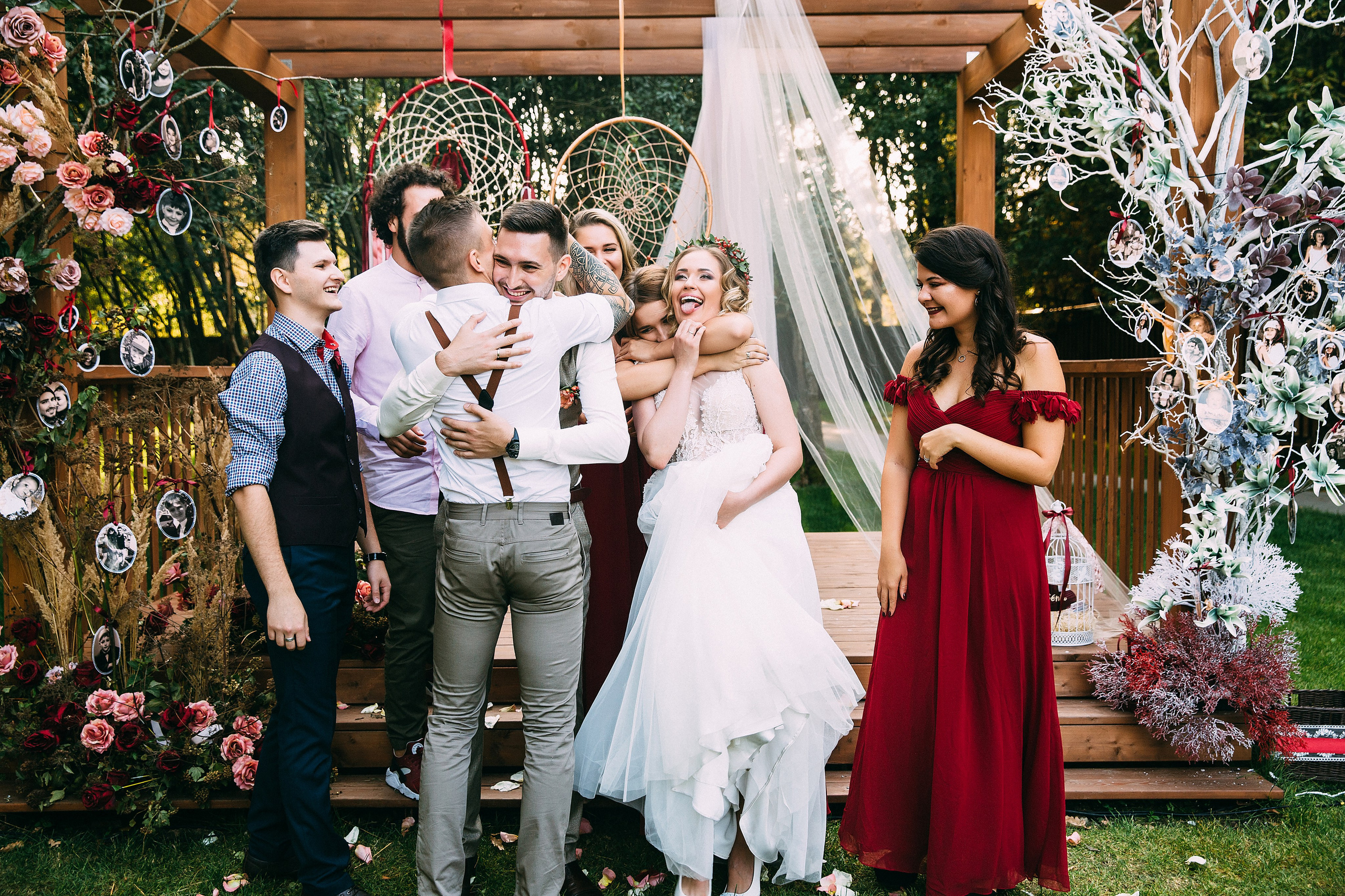 Молодожёны стоят под свадебной аркой в коттеджном посёлке Подмосковья, их поздравляют друзья. Все улыбаются, обнимаются и радостно смеются. Искренние эмоции свадебного дня.