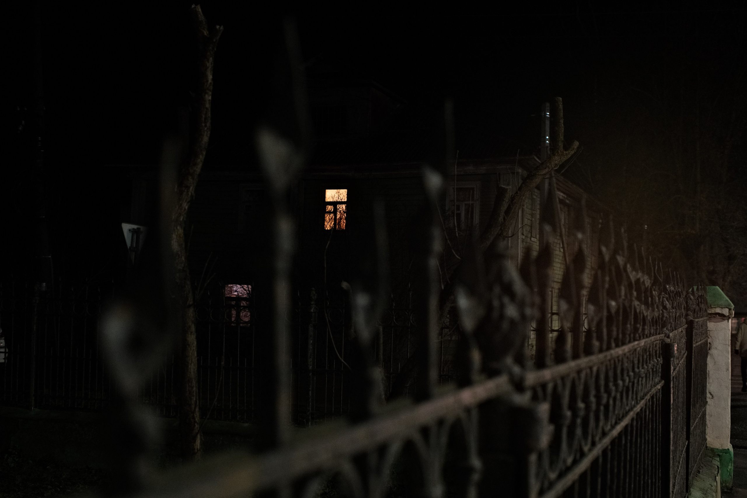 Ночной деревянный дом с освещенными окнами за металлическим забором, Переславль-Залесский, атмосферное фото между сезонами