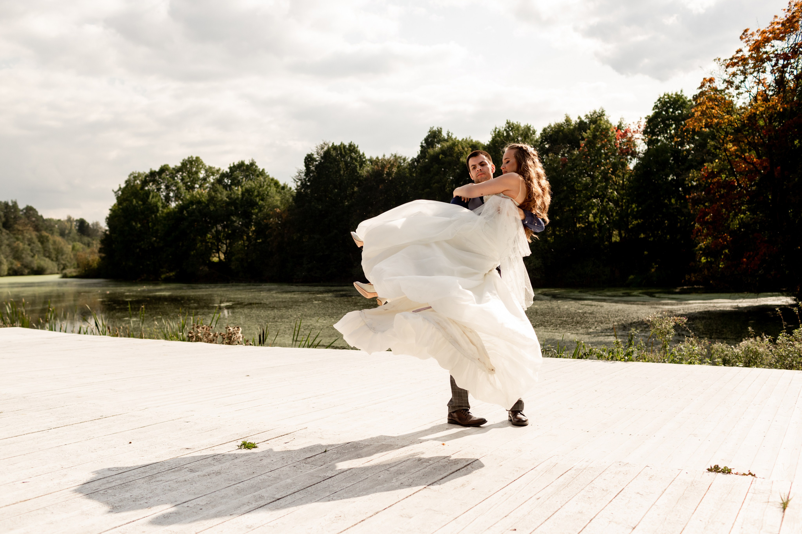 Жених кружит невесту на руках около озера.