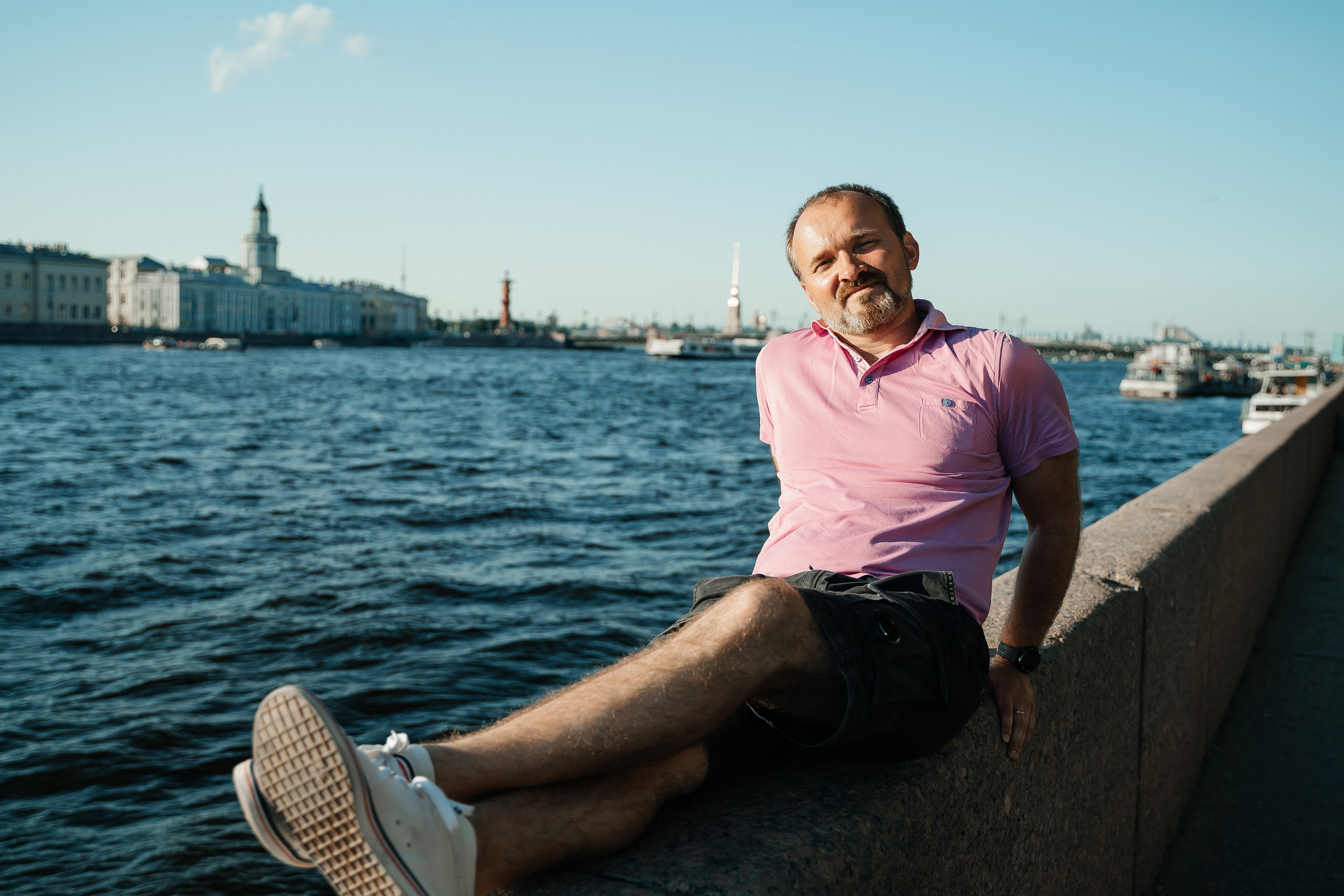 Красивая фотография мужчины отдыхающим на камне с видом на Неву и Дворцовый мост