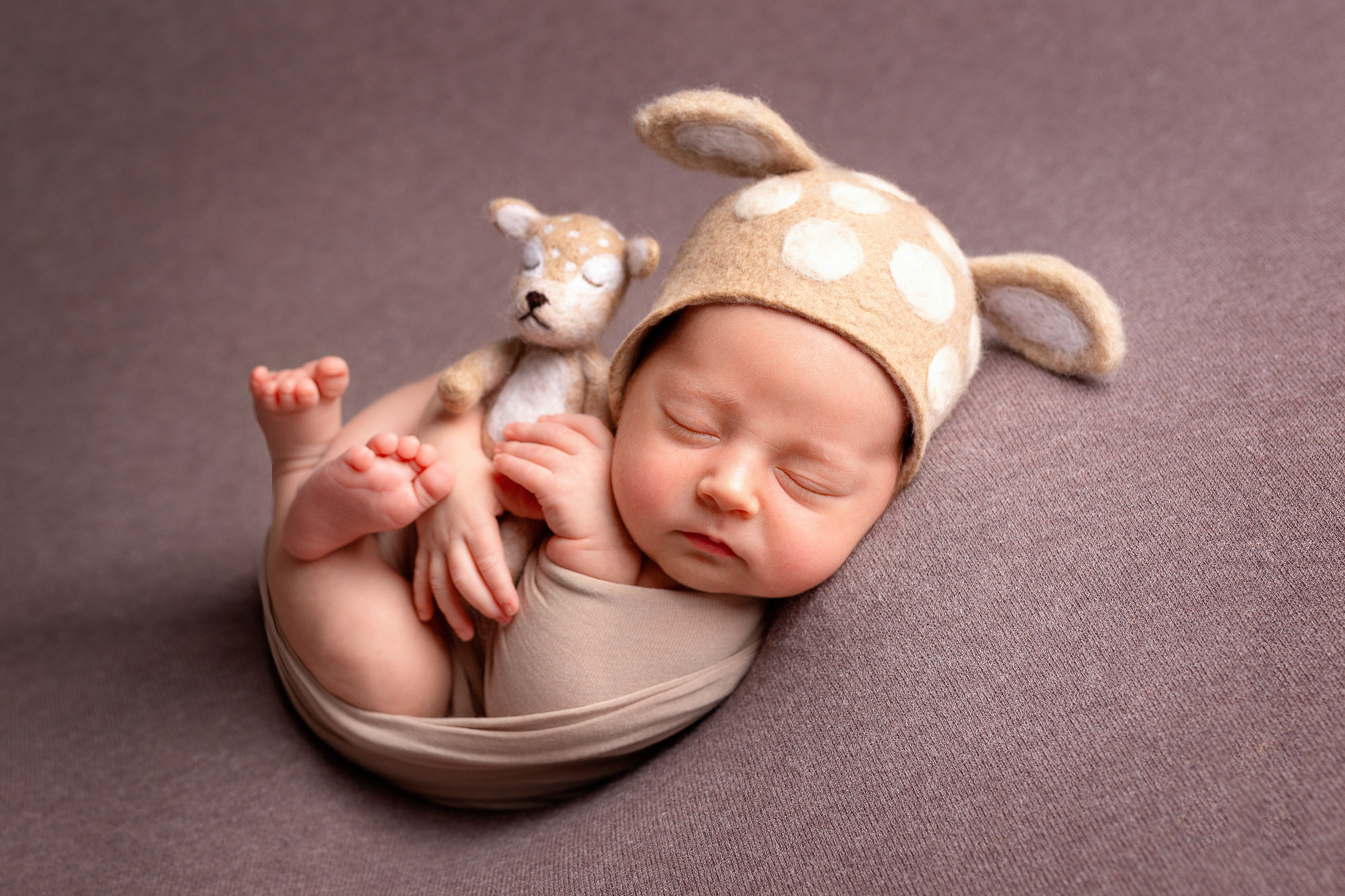 Новорожденный мальчик в образе оленёнка с игрушкой на коричневом фоне.