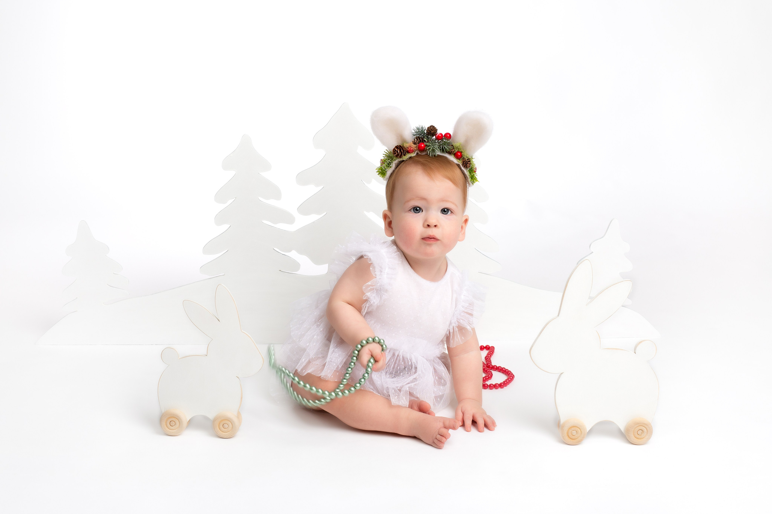 Восьмимесячная девочка в образе зайки играет с бусами.