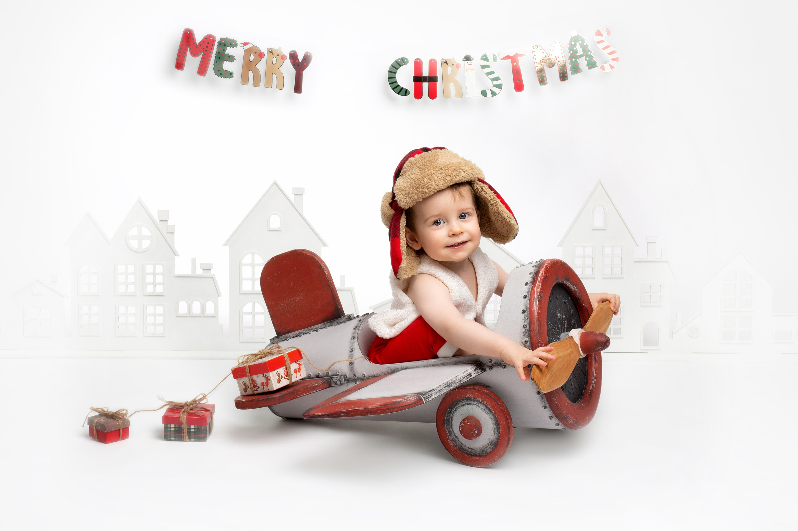 Годовалый мальчик в зимней шапке в сером самолёте с винтом.