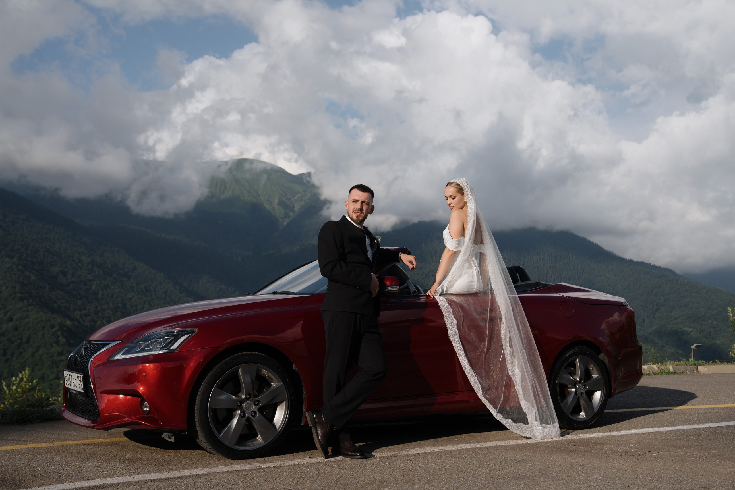 Жених и невеста у красного кабриолета Lexus на фоне гор Красной Поляны