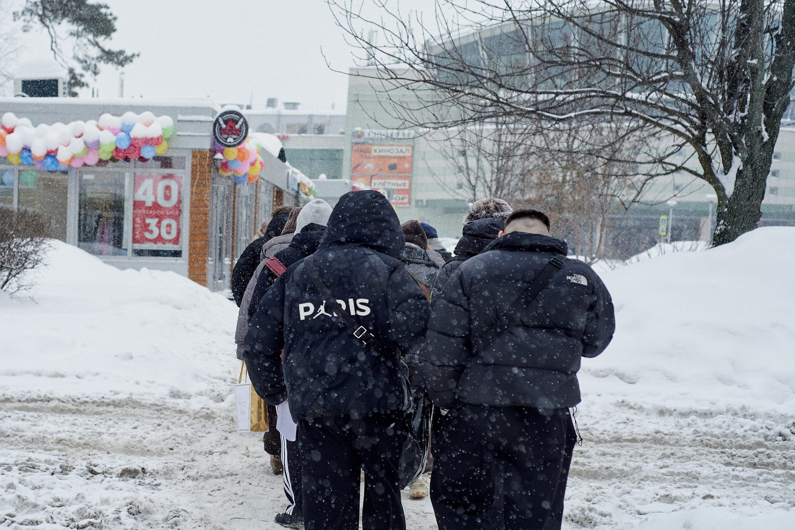 Young people without hats in winter snowfall. Young adults walking along a snowy street in Russia during active snowfall.