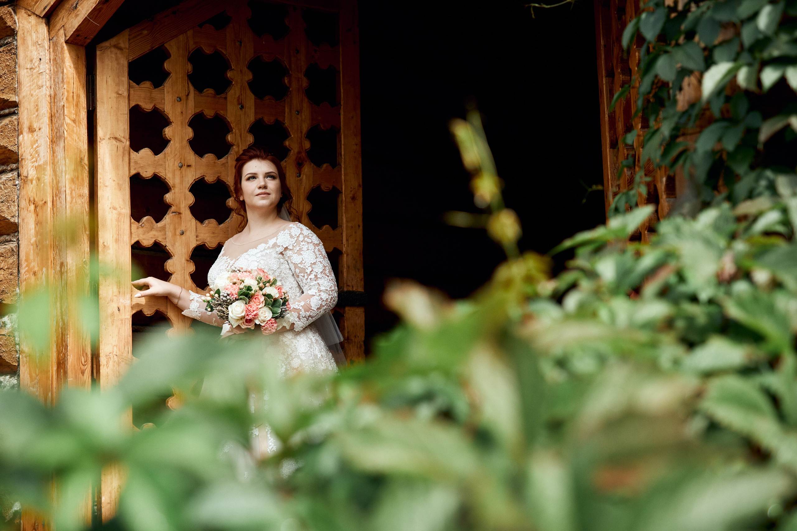 Фотосессия свадьбы в Измайловском кремле перед росписью - пример фотографии с невестой в белом платье и букетом в руке на фоне красивых стен кремля из массива дерева