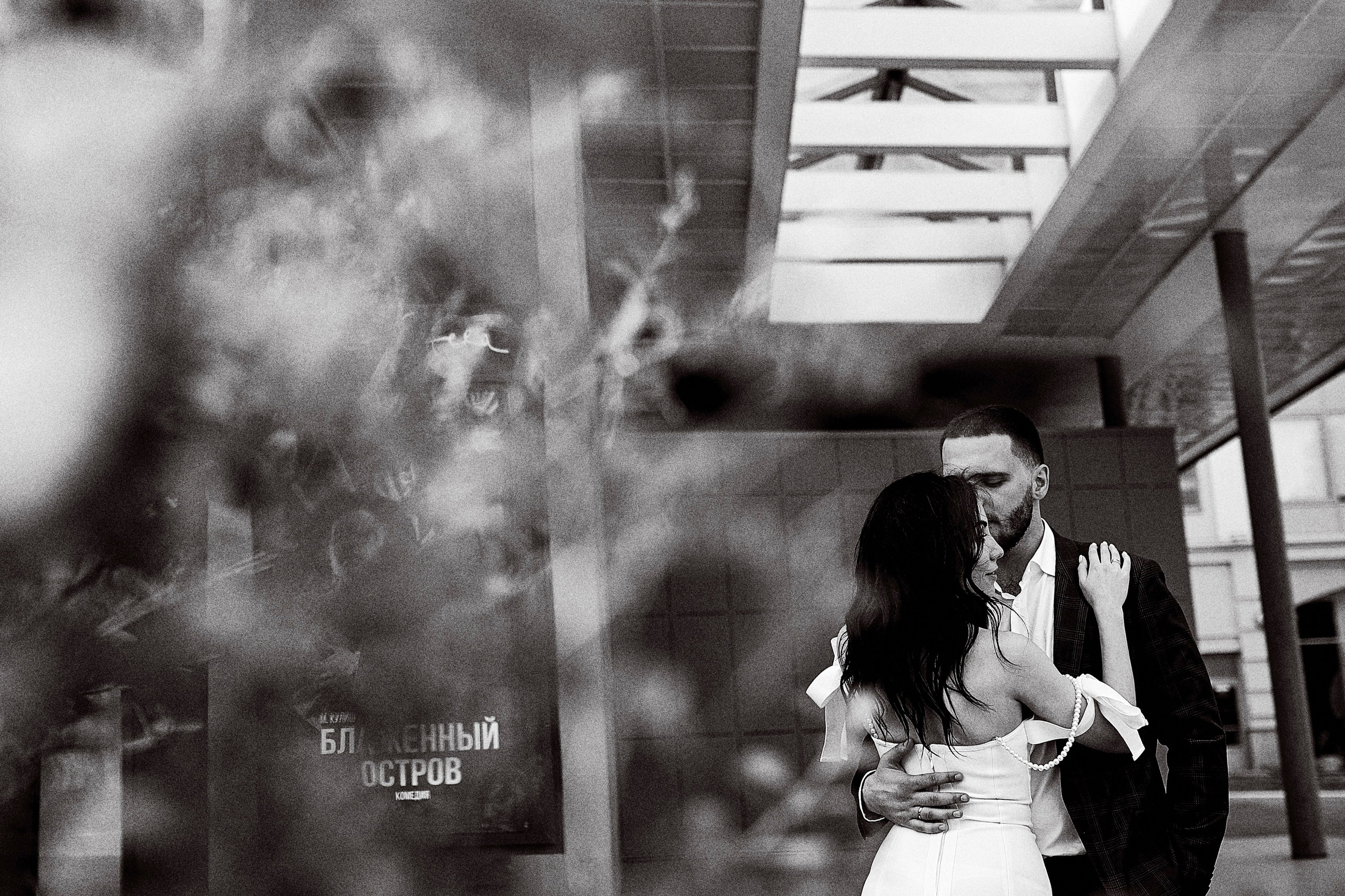 Фотограф на роспись делает снимок молодоженов в центре города в Москве – красивая черно-белая фотография целующейся молодой пары на фоне массивных конструкций здания