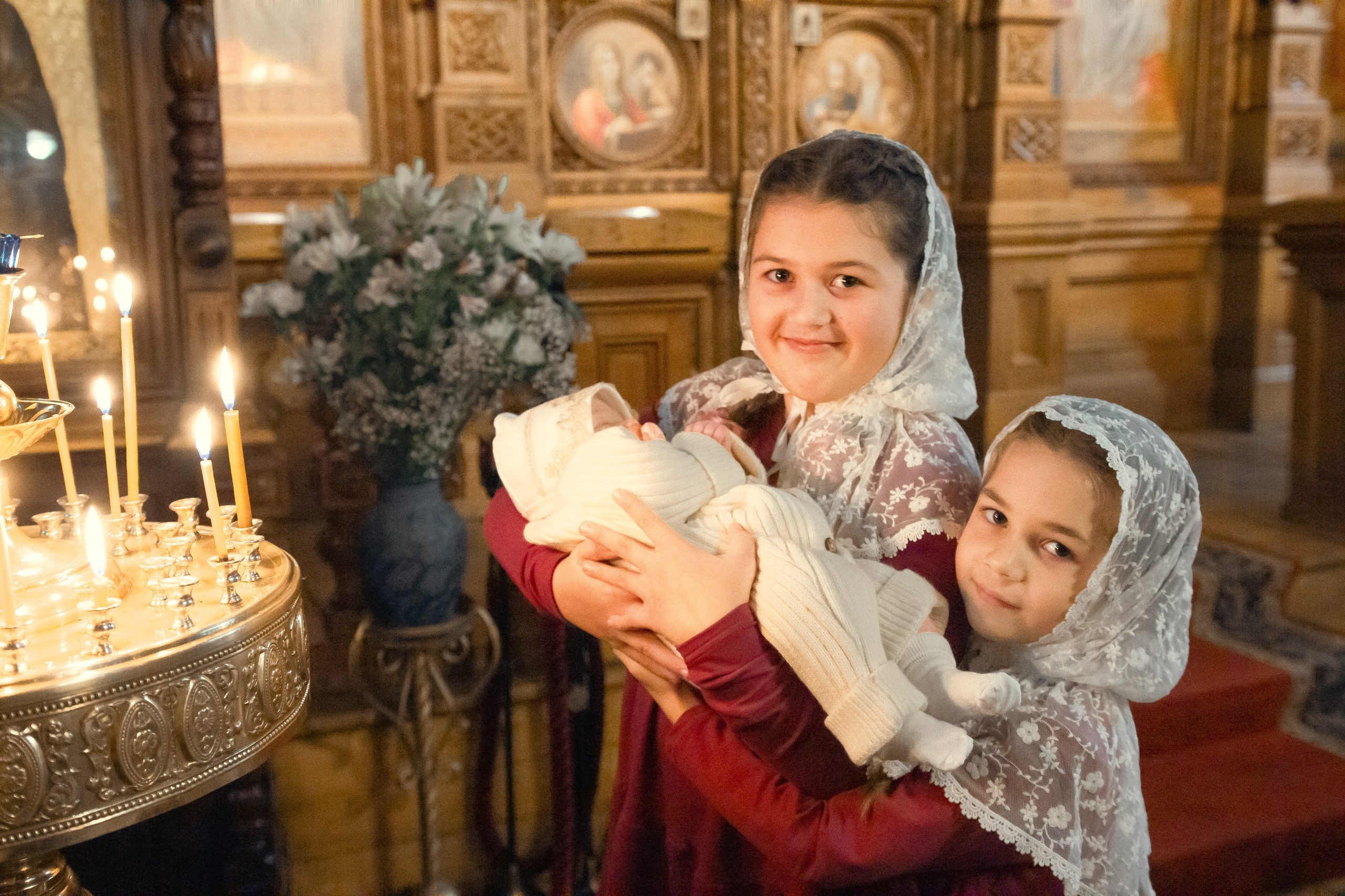 Храм, церковь, православие, крещение, таинство, свечи, алтарь, съемка в храми, съемка крещения. Момент крещения младенца в храме. Священник держит ребенка над чашей с водой, окруженный родителями и крестными. Вокруг видны святые иконы, а свет мягко проникает через окна, создавая атмосферу глубокого уважения и духовности.