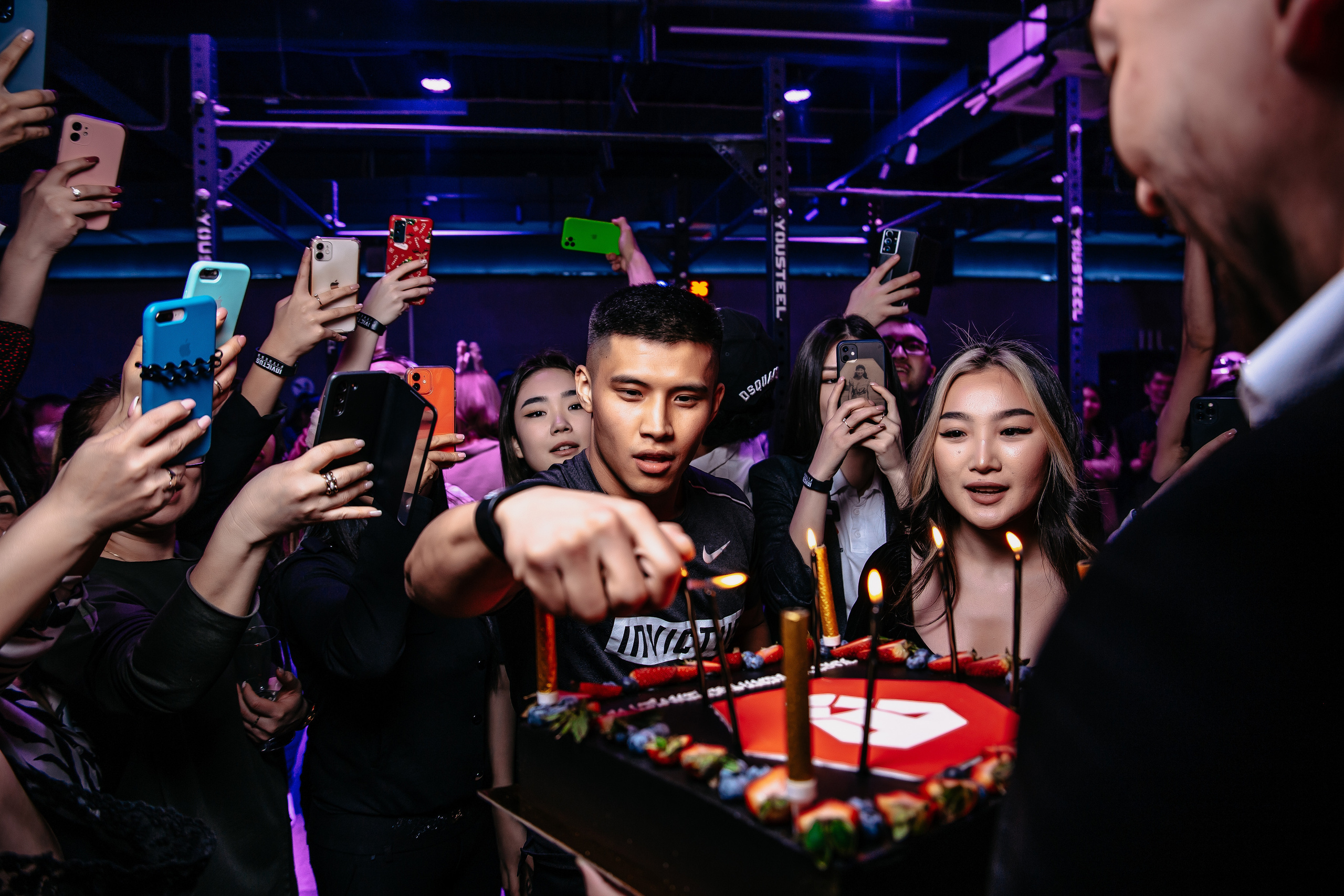 День рождения в спортивном комплексе. Мужчина поджигает свечи на торте.