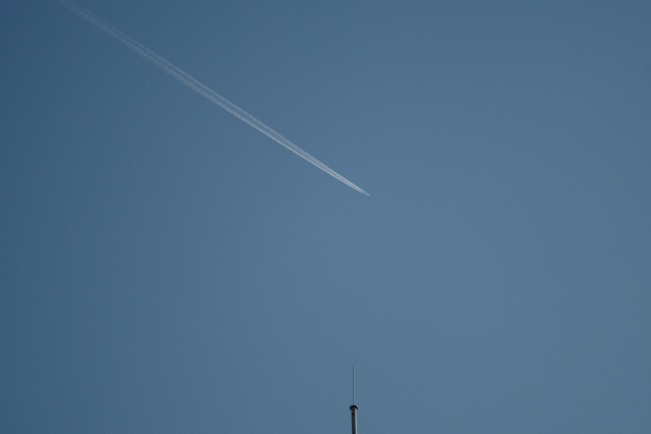 Минималистичная фотография: белый след самолёта на голубом небе, диагональная композиция, антенна внизу, цветное фото, чистое небо