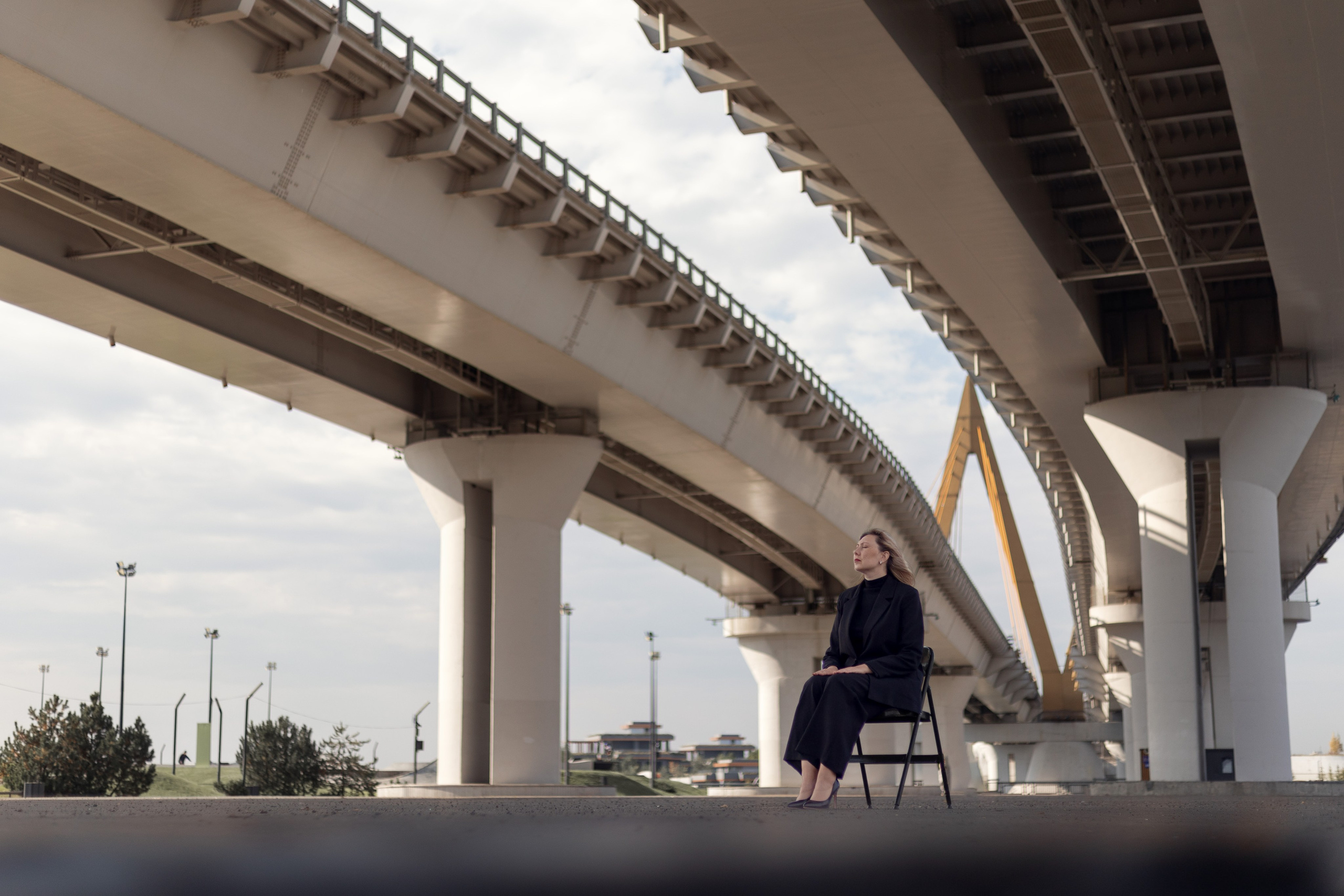 Психолог в чёрном костюме сидит под мостом Миллениум в Казани — деловая фотосессия для соцсетей