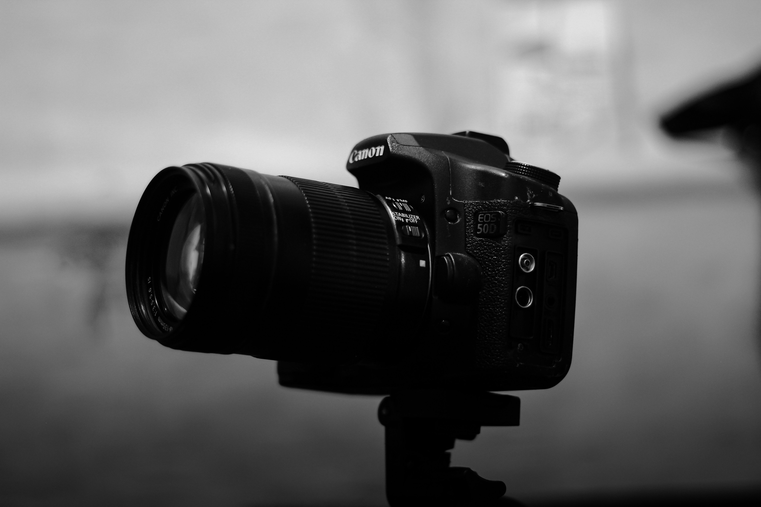 A black Canon EOS 50D camera with a zoom lens, set against a blurred background