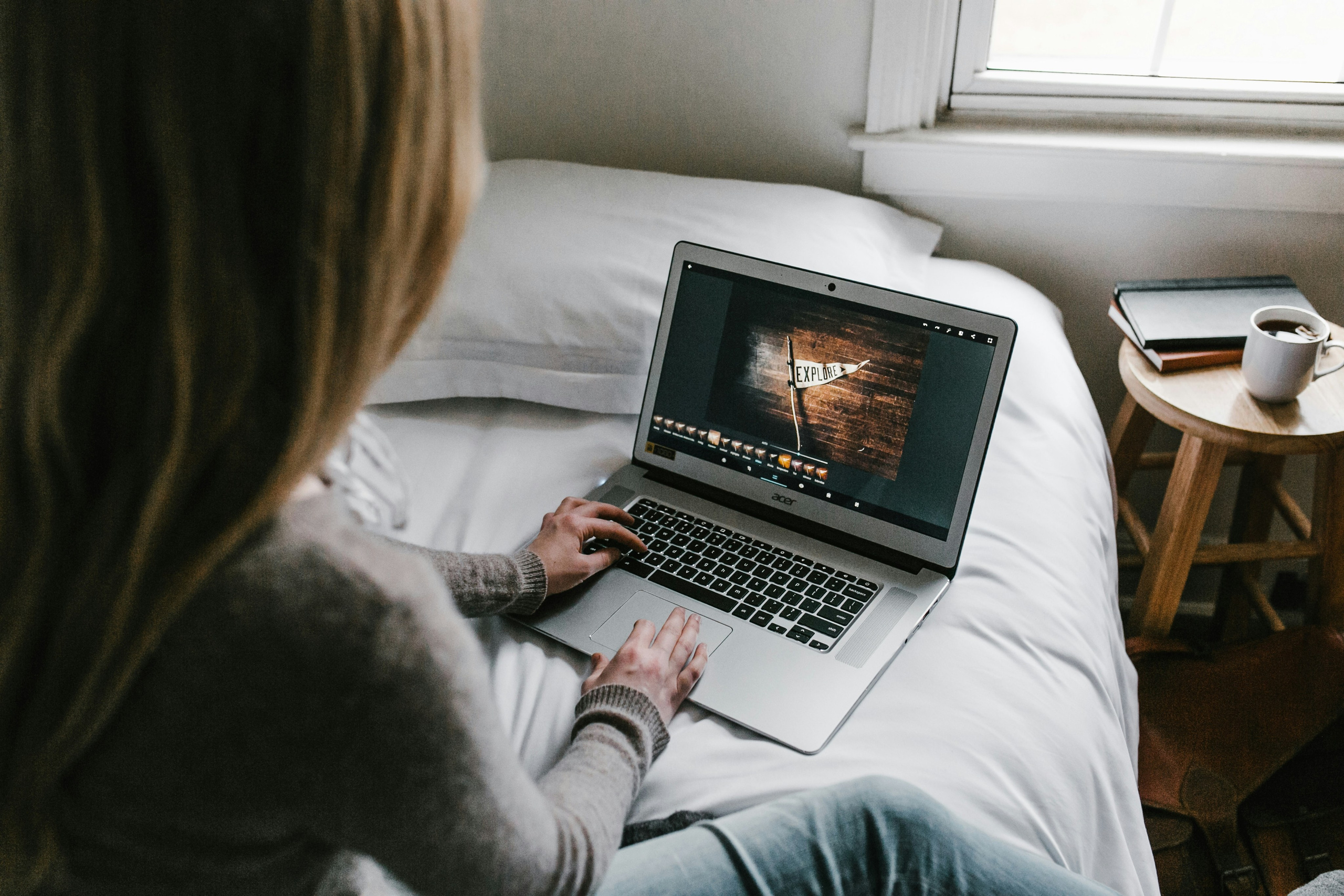 A person edits a photo on a laptop while sitting on a bed, focusing on the screen