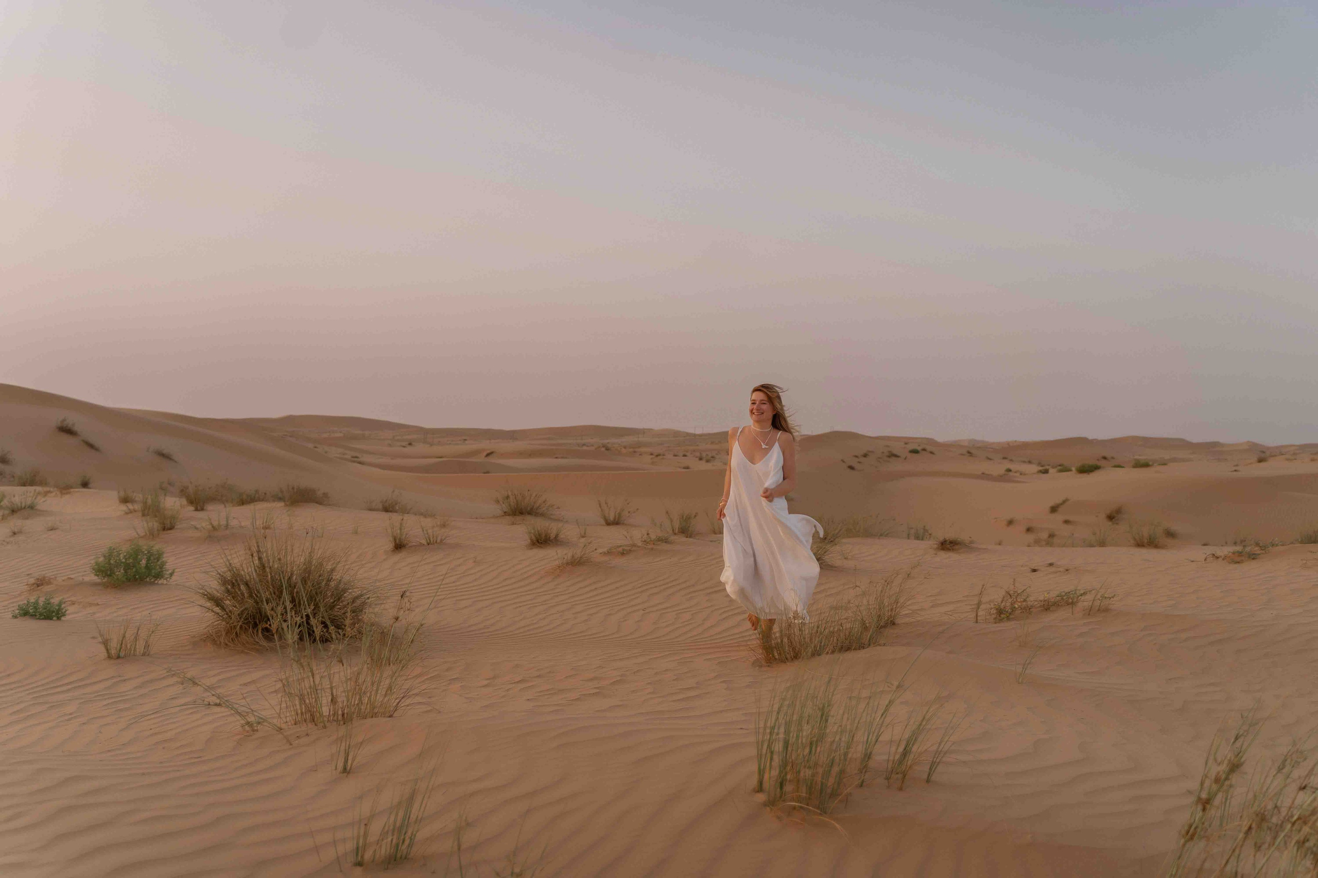 Woman in a white dress walking in desert in Abu Dhabi