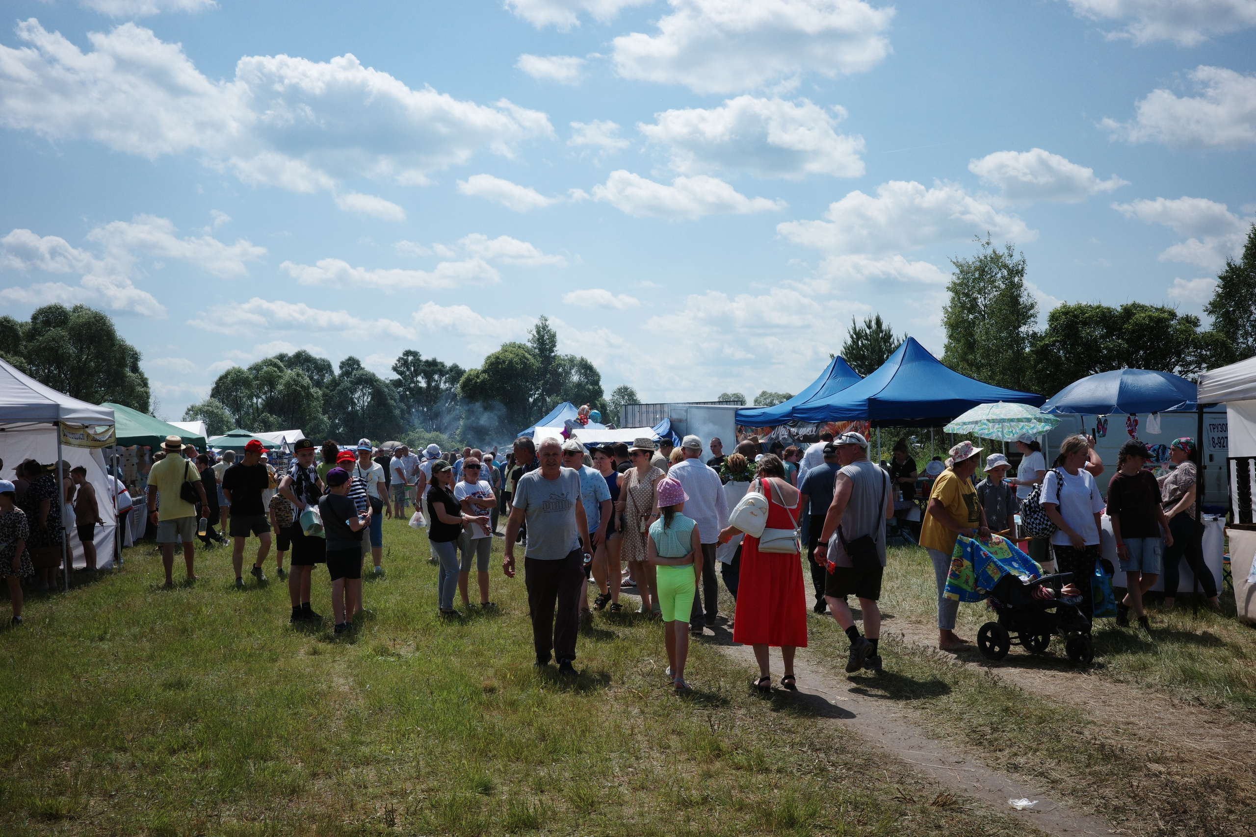 Плотная толпа на фестивальном поле, дым от мангалов, шатры, синий шатёр вдали