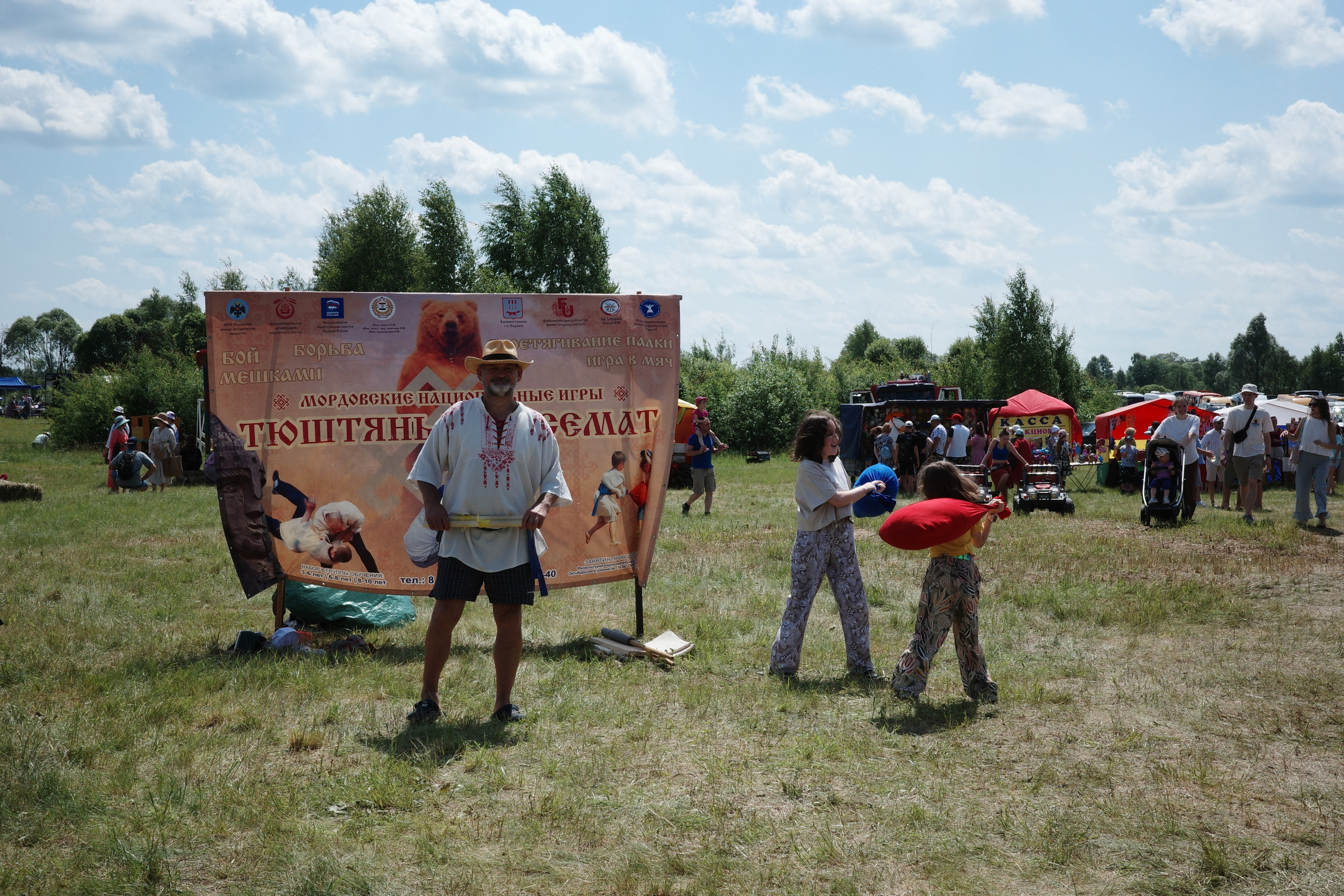 Баннер Мордовских национальных игр Тюштянь Кемат, участник в народном костюме, дети играют рядом
