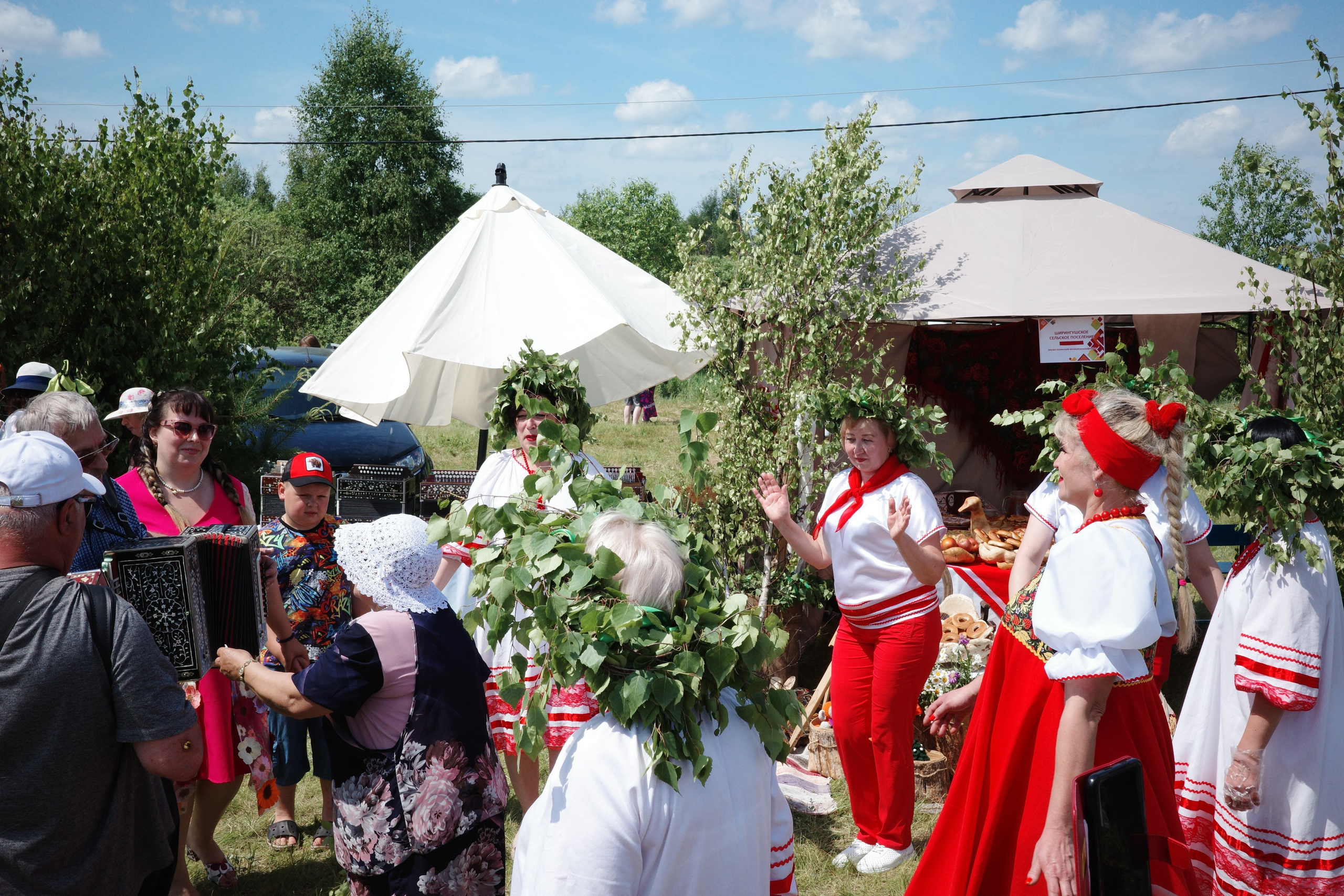 Хоровод с гармонистом, люди в народных костюмах держатся за руки и танцуют на открытом поле