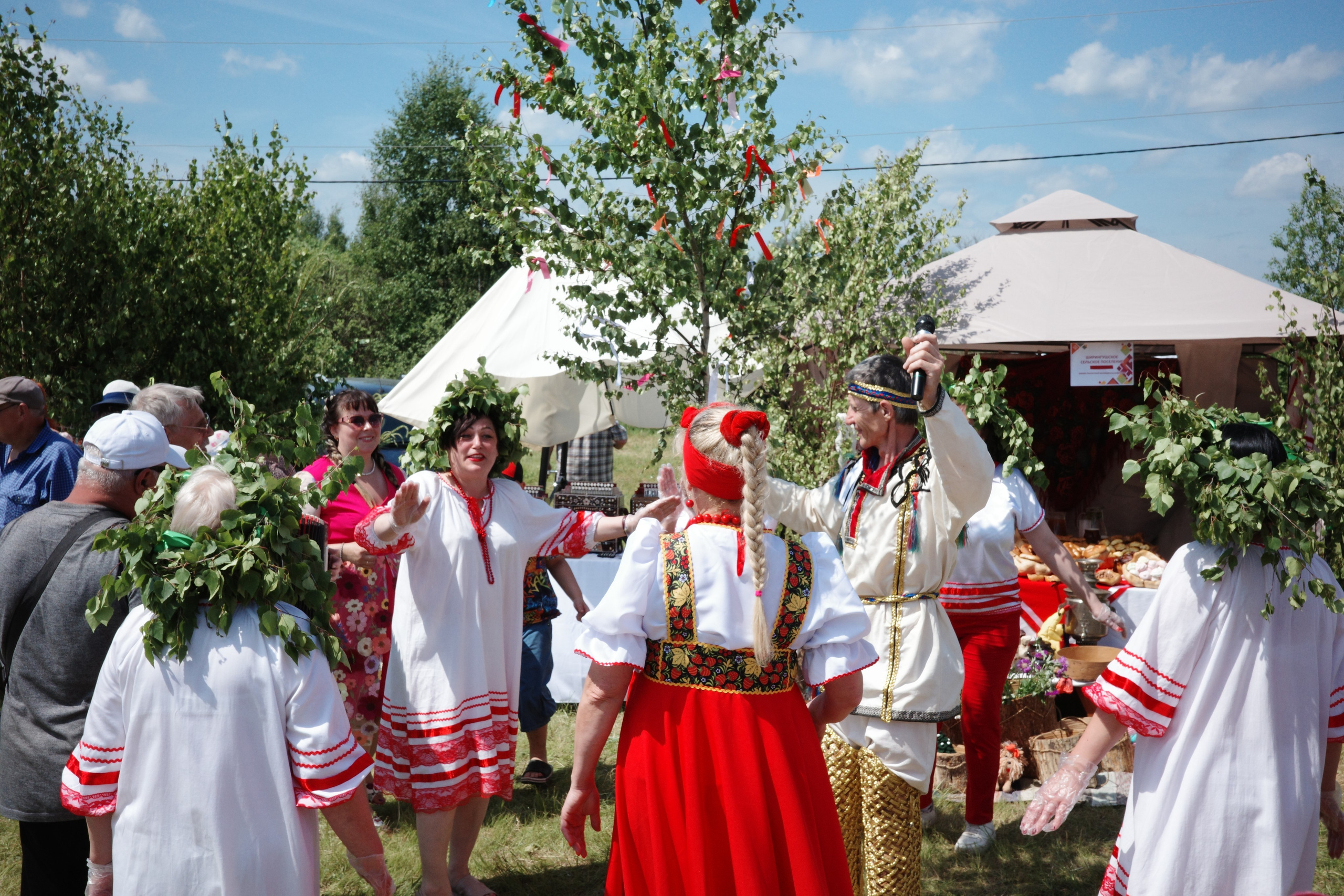 Хоровод вокруг украшенной красными лентами берёзы, участники в народных костюмах с берёзовыми венками