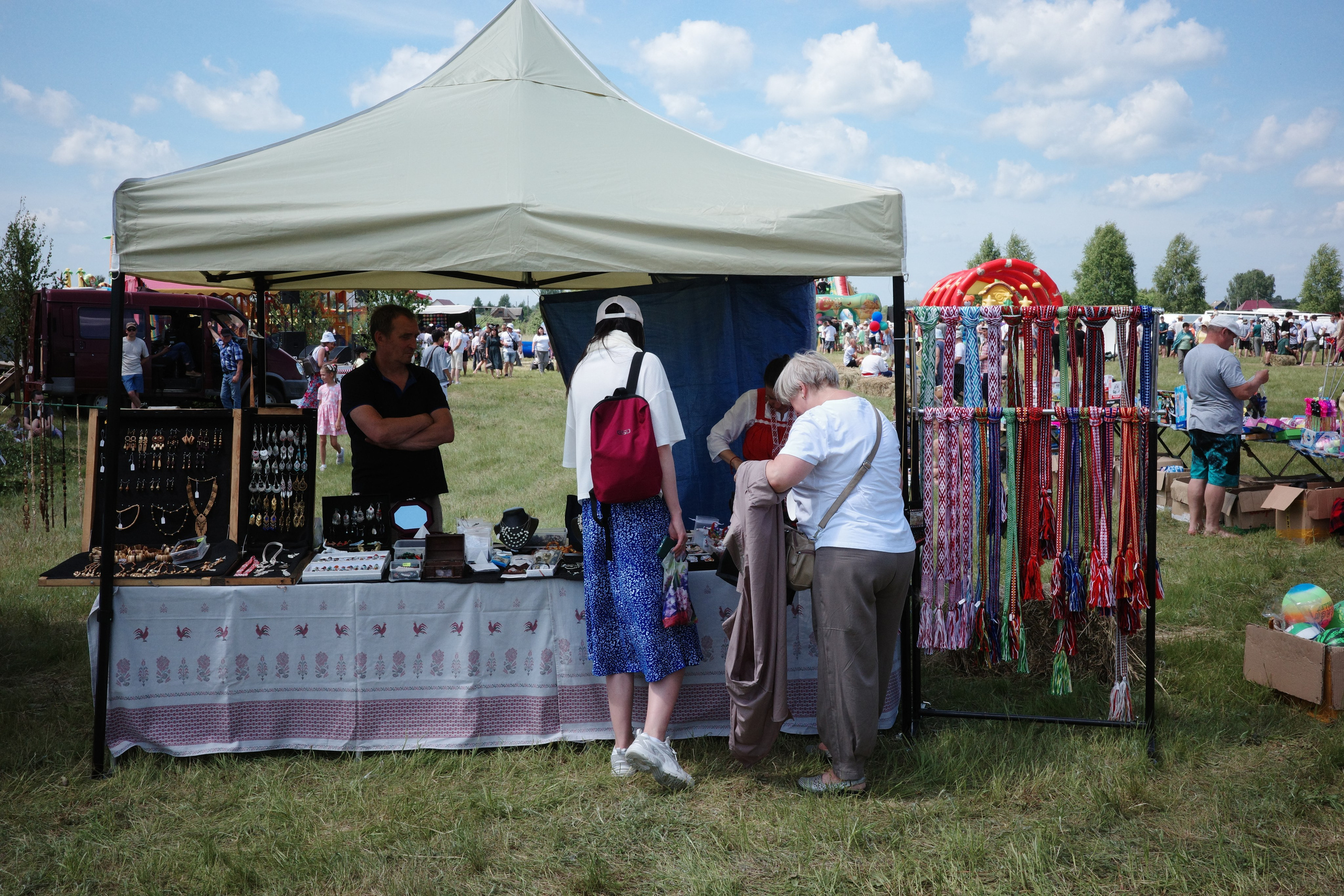 Сувенирный шатёр с бижутерией ручной работы и разноцветными нитями, покупательница рассматривает украшения