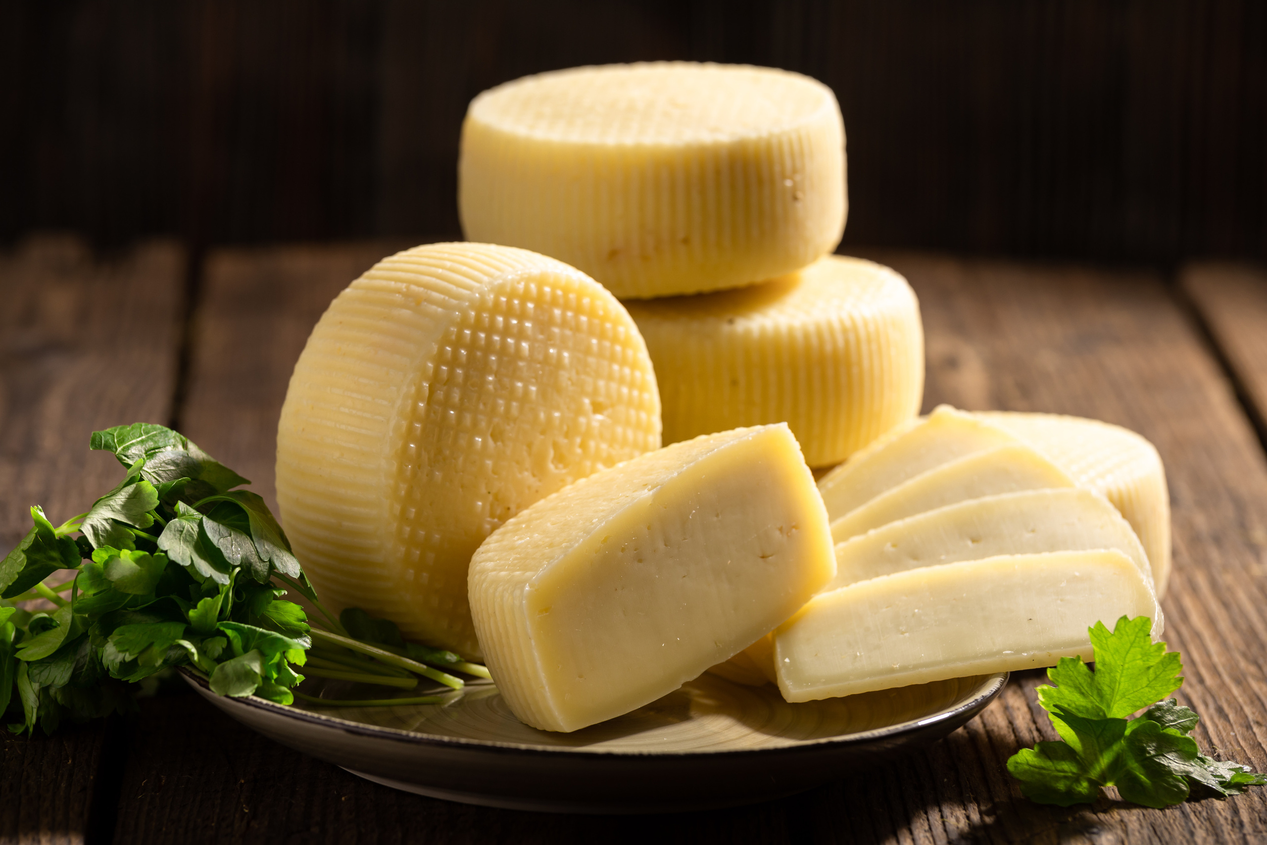 Несколько головок сыра качотта на тарелке с зеленью, одна головка нарезана. На фоне состаренных досок.