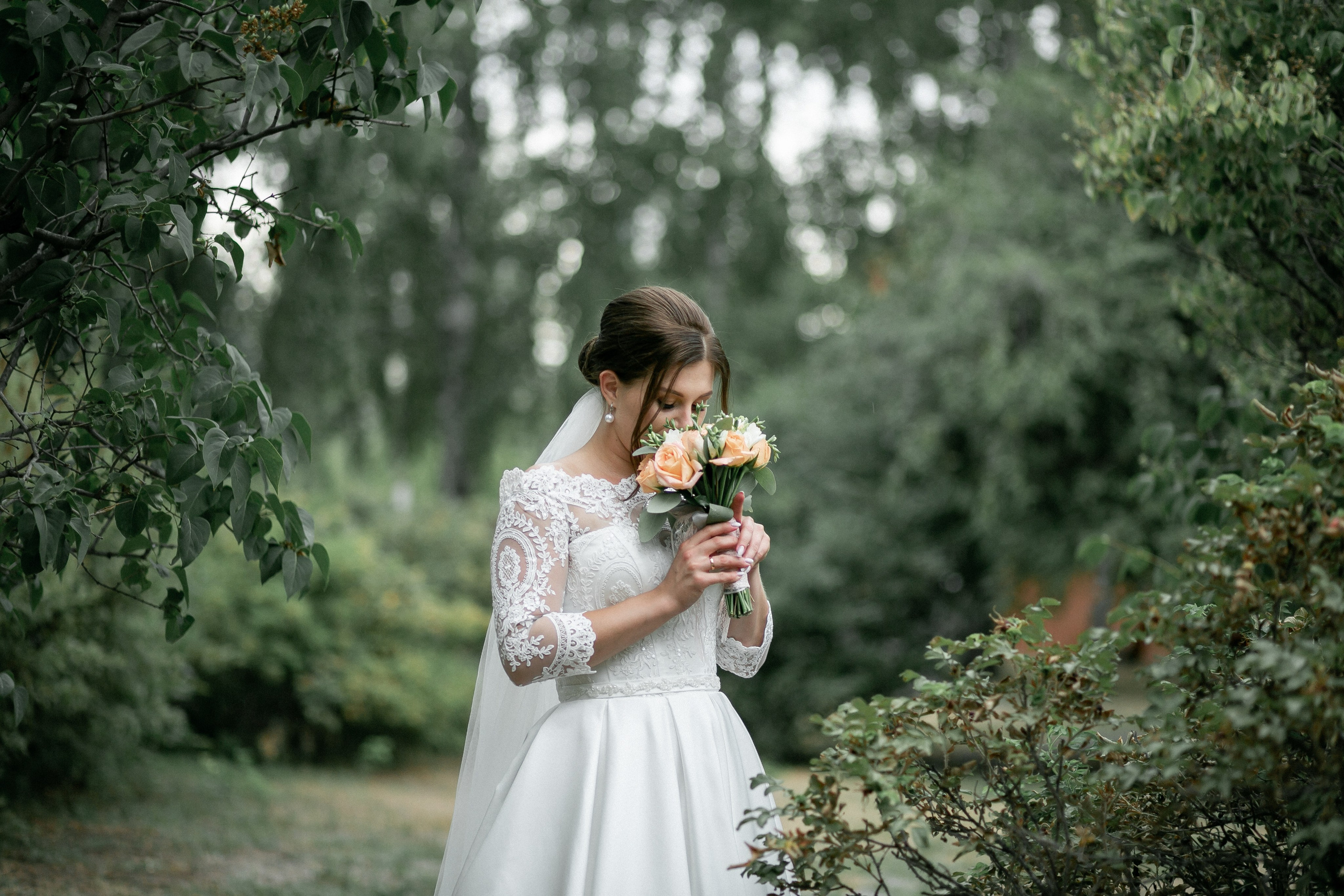 Невеста стоит в парке и держит букет в руке