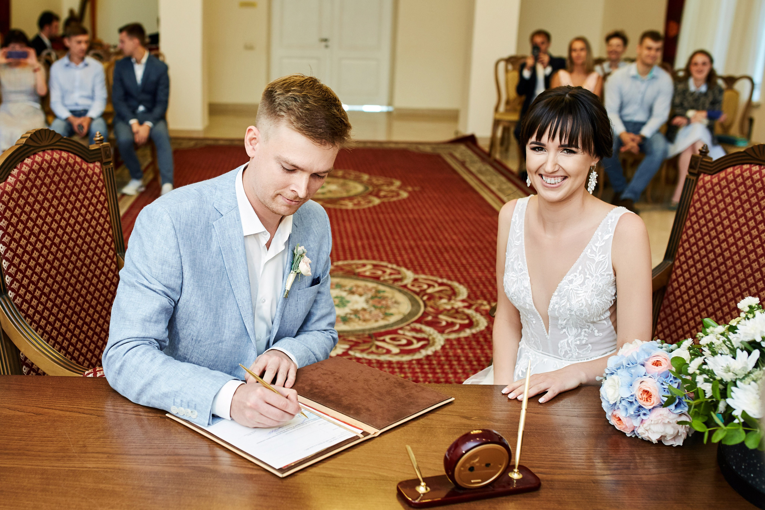 Фотограф в ЗАГСе сделал фото расписавшихся молодоженов в Дворце бракосочетания на ВДНХ – получилась яркая фотография молодоженов, где муж в небесно-голубом костюме ставит роспись, а невеста в роскошном белом платье ярко улыбается