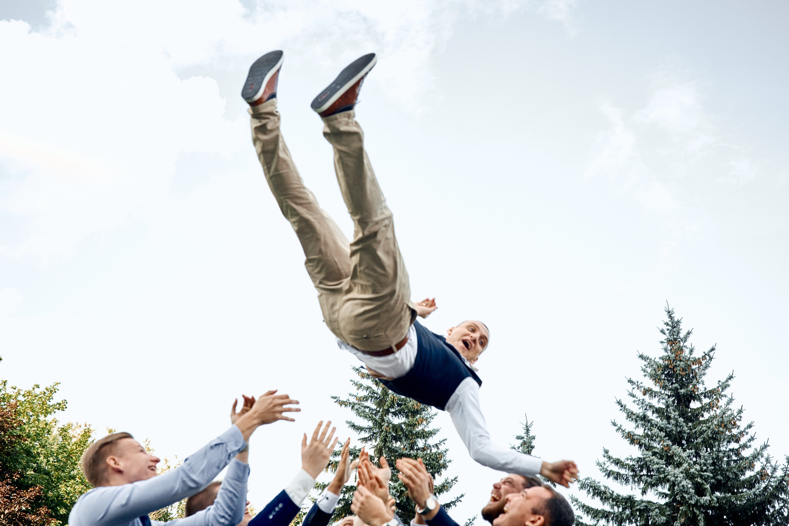 Свадебный фотограф проводит летнюю фотосессию в Москве для молодоженов в парке ВДНХ – фотография жениха, которого подбрасывают друзья