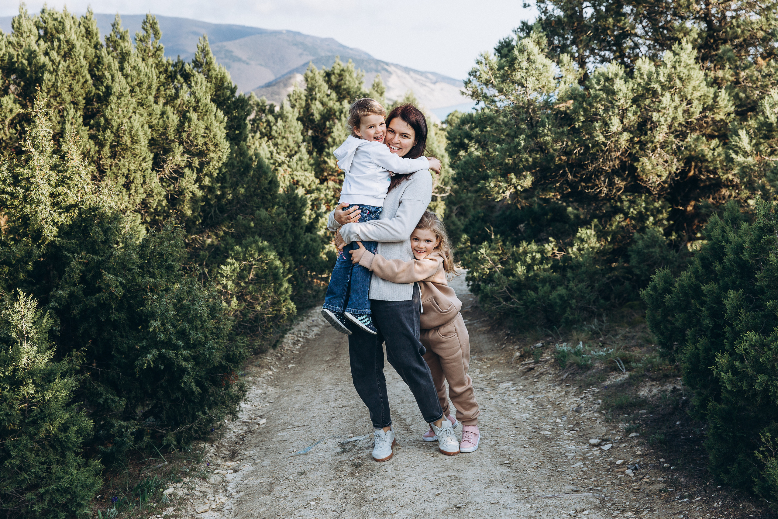 Молодая мама обнимается с двумя дочками в лесном пейзаже