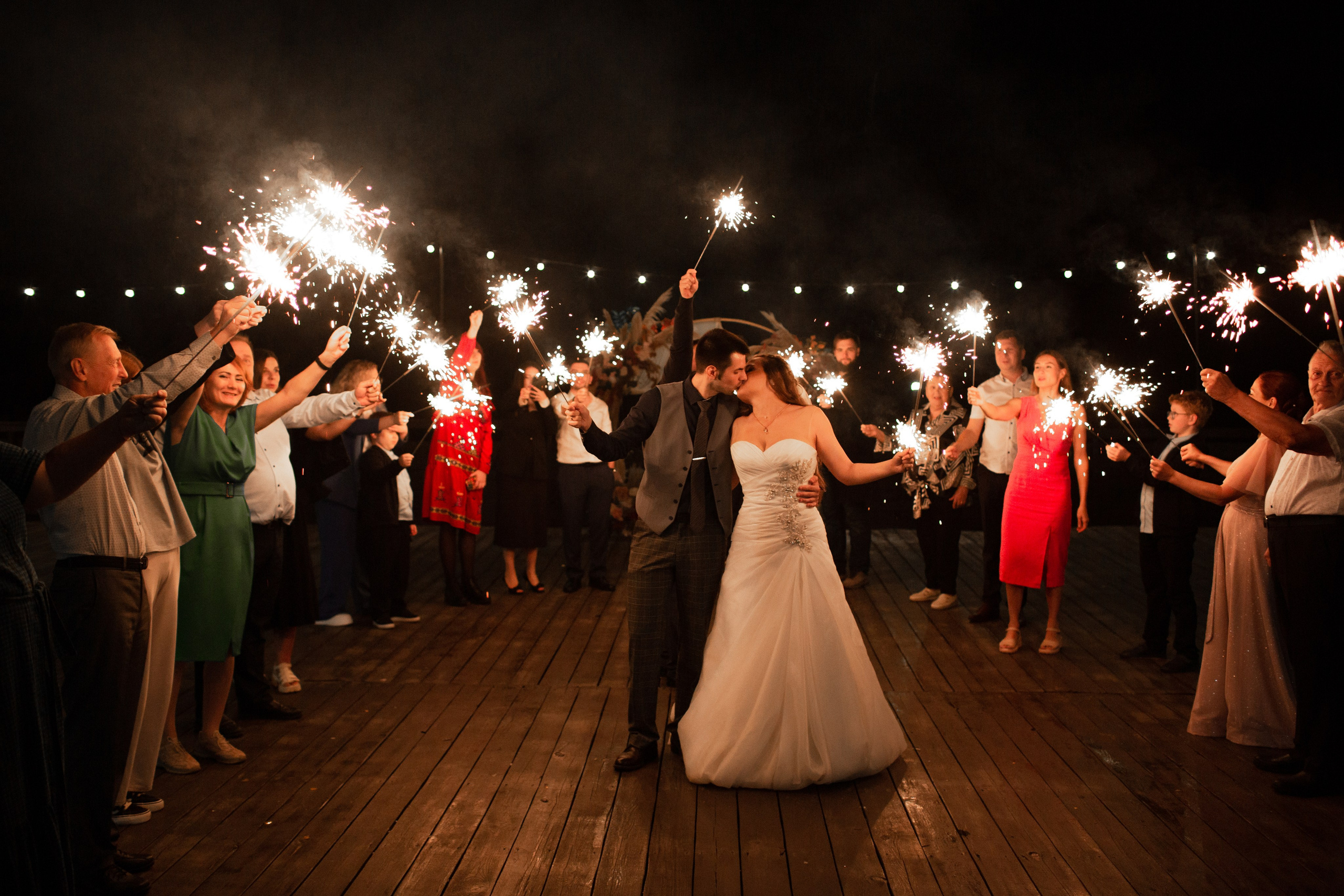 Бенгальские огни на завершении свадебного дня: гости держат огни кругом вокруг молодоженов.