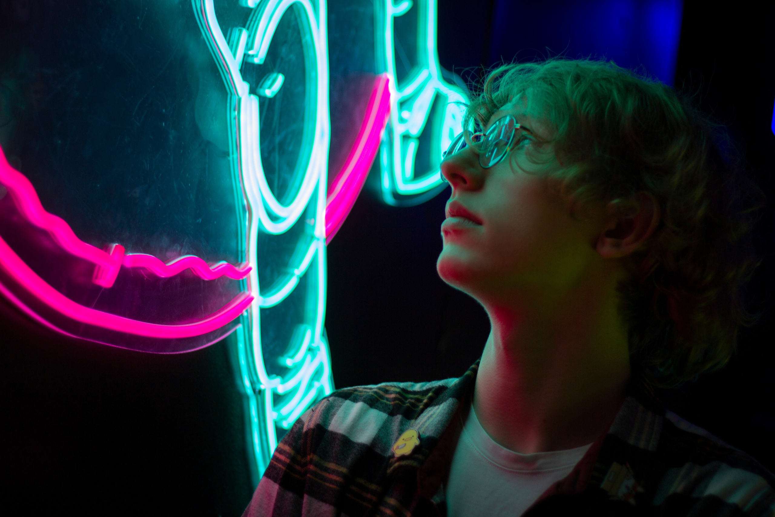 Кудрявый парень в очках смотрит на неоновую вывеску