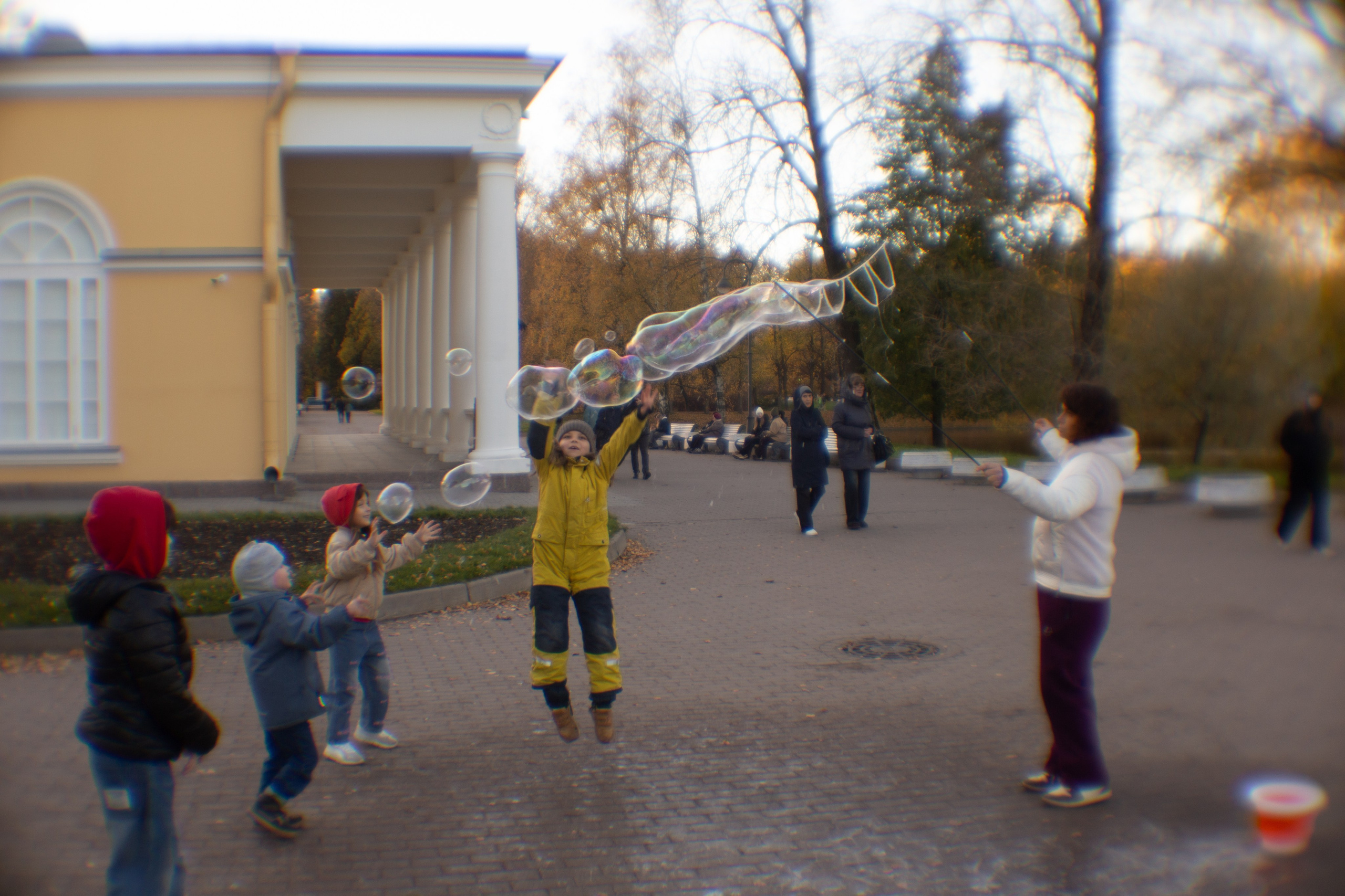 Художественная фотография в Парке Победы Санкт-Петербурга: размытые фигуры детей, ловящих мыльные пузыри на аллее, съёмка творческим объективом, идеи для фотосессии на природе в СПб