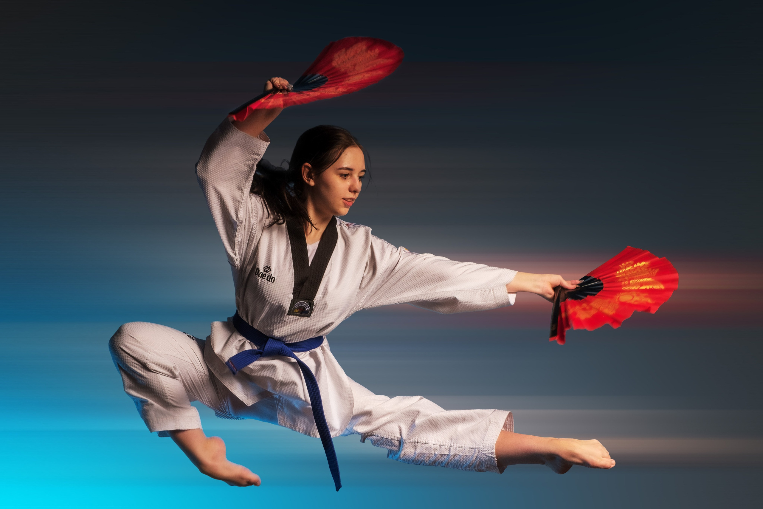 Девочка в боевом кимоно в прыжке и с двумя веерами в руках