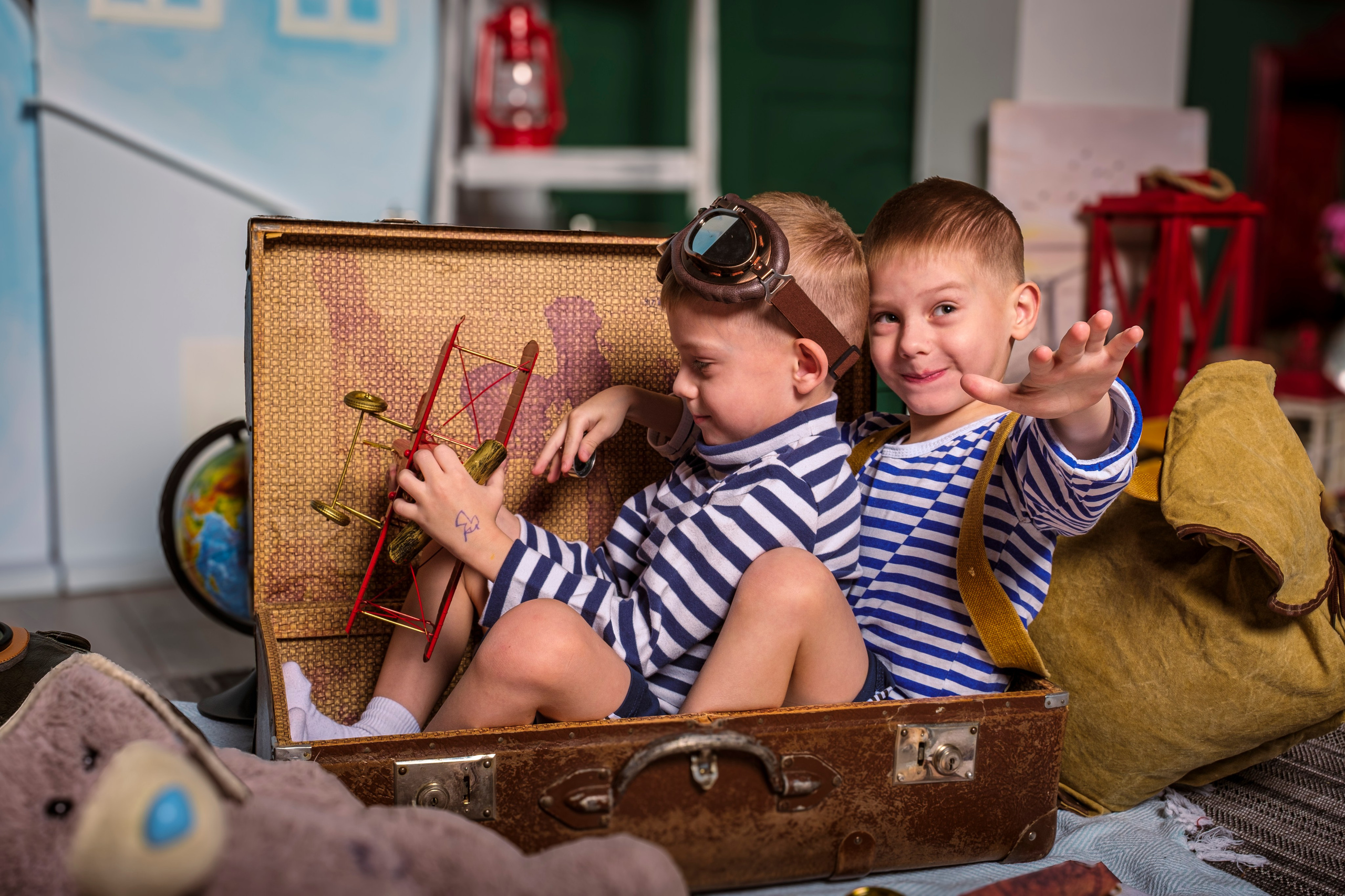 Два малыша-мальчика играют с игрушками сидя внутри чемодана