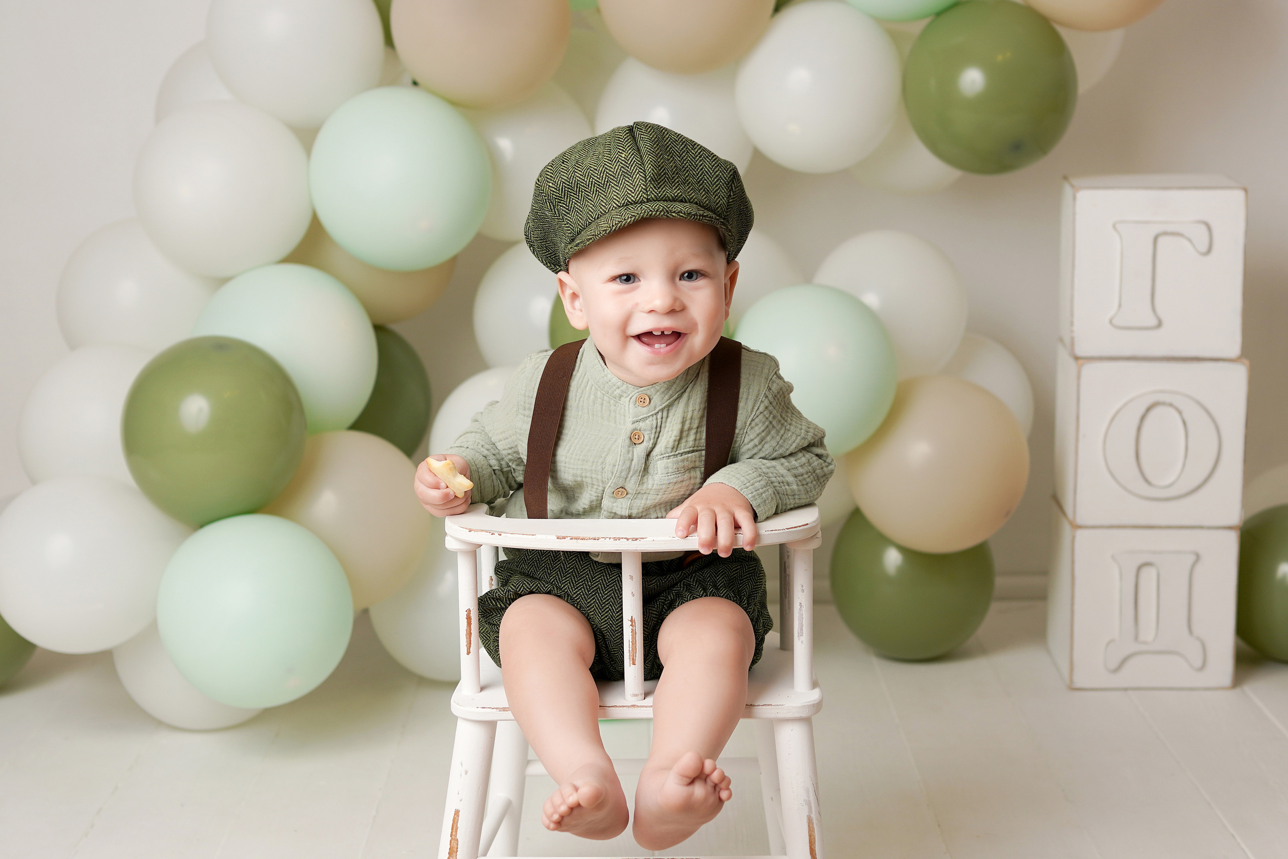 Малыш с родителями приехал на детскую фотосессию «Первый годик», на фото он сидит на стульчике, рядом зеленые шарики и огромные кубики Год.