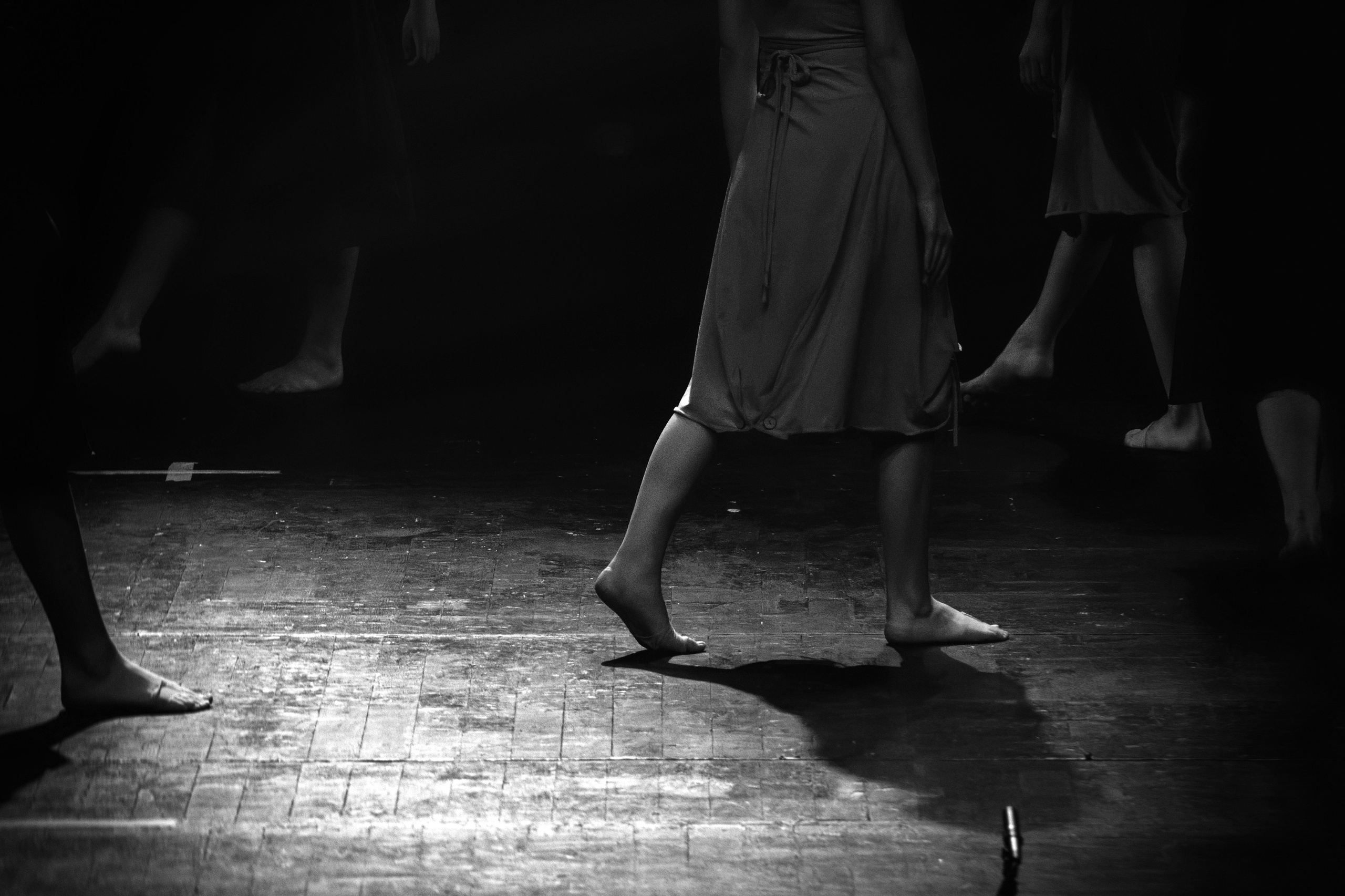 Деталь босых ног танцоров на деревянном полу сцены, драматичное освещение, минималистичная композиция