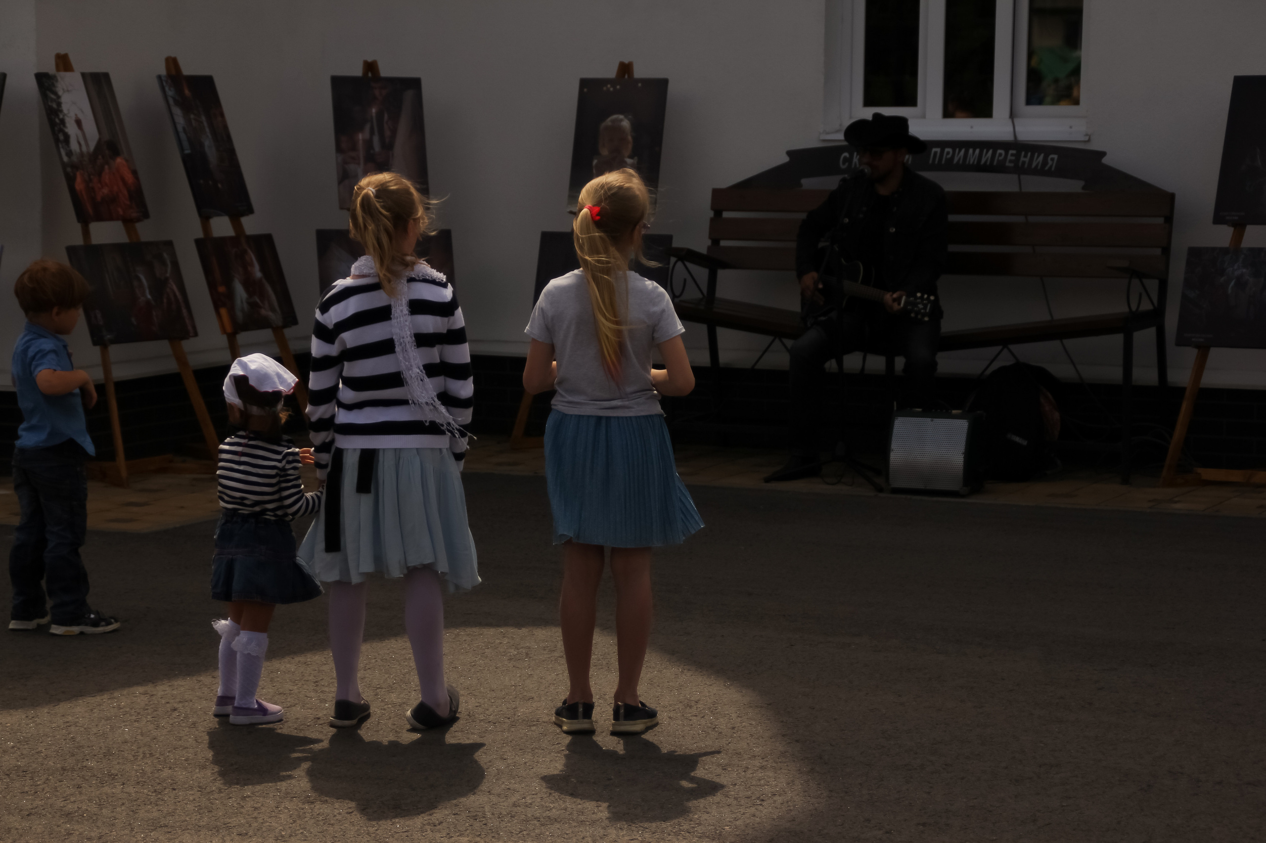 дети на фотовыставке слушают как поет и играет гитарист на детей красиво падает луч света и дает их тень