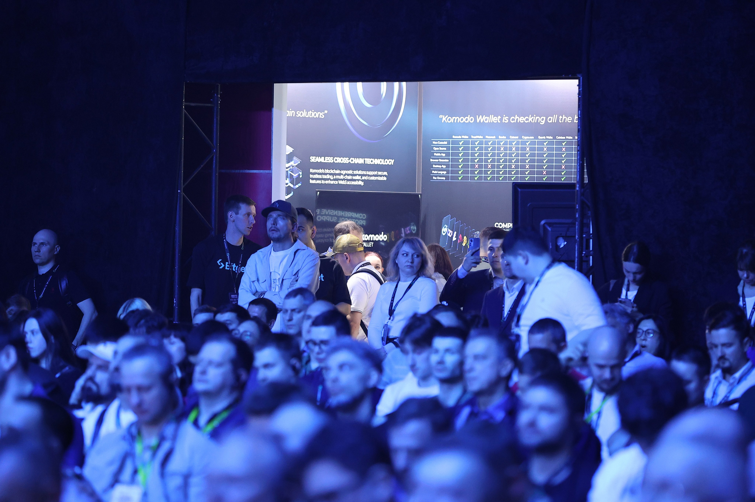 Зрители в зале внимательно смотрят на сцену, на заднем плане арка с выставкой и живым общением с торговыми представителями.