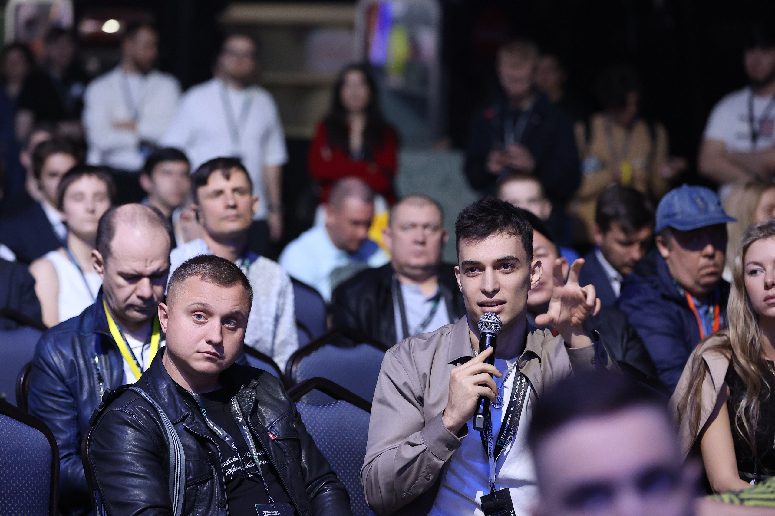 Зритель задает вопрос спикерам, держит микрофон, остальные зрители внимательно слушают.