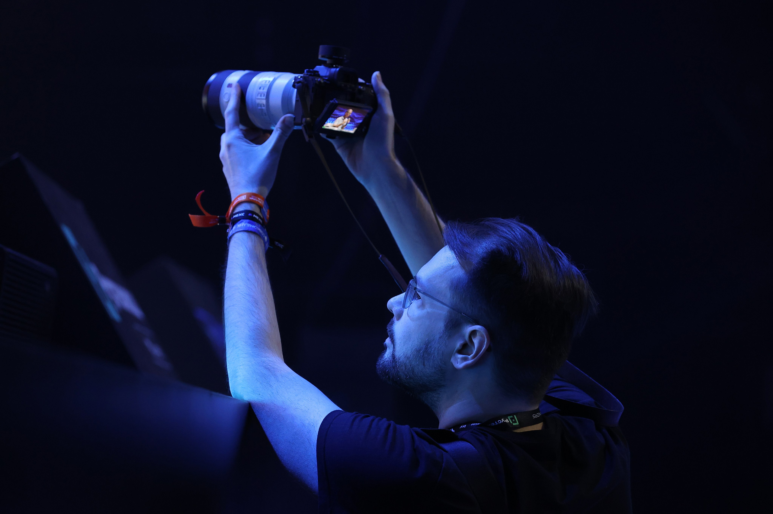 Темное фото: фотограф фиксирует процесс, камера наводится на сцену, видно, как снимается мероприятие.