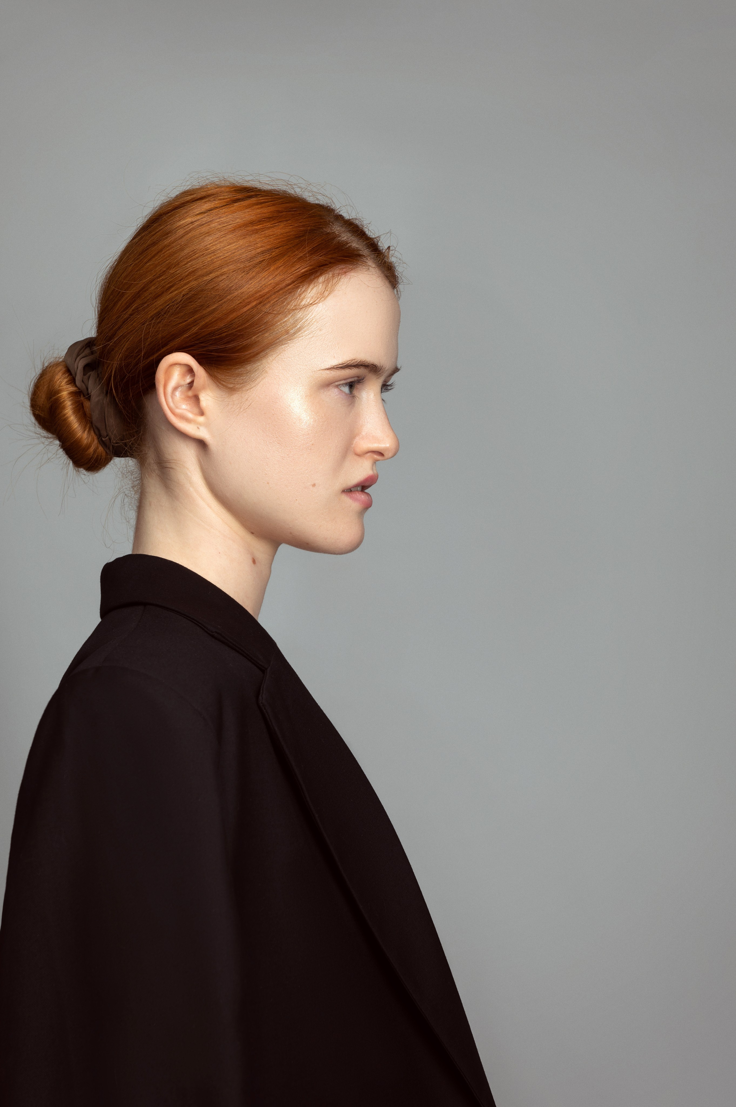 Студийная съемка модельных тестов. Рыжая девушка в черном пиджаке в профиль